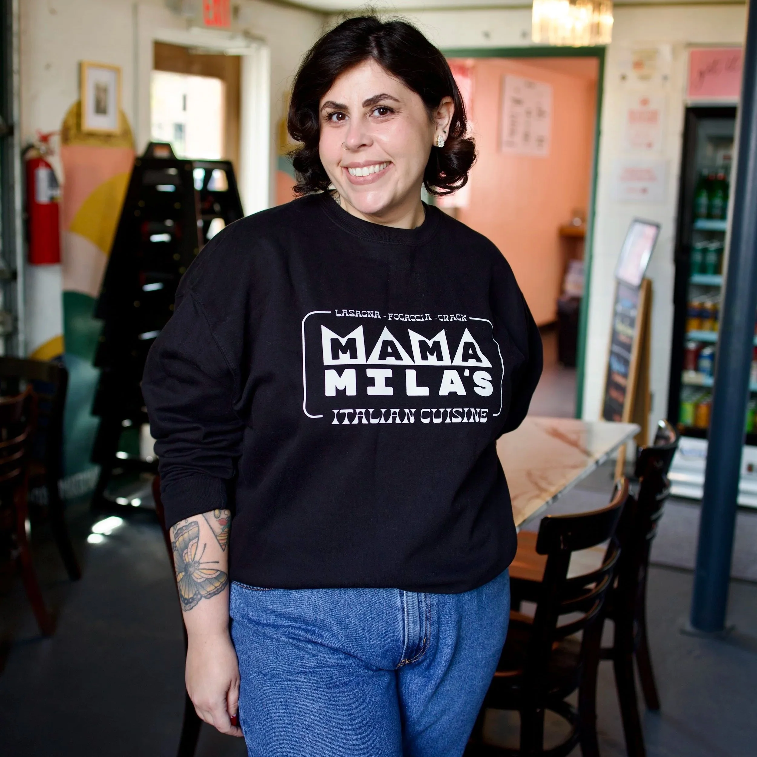 Mila wearing the Black sweatshirt with a white vintage Mama Mila's design on it, featuring the words Focaccia, Lasagna, Crack and Italian Cuisine"