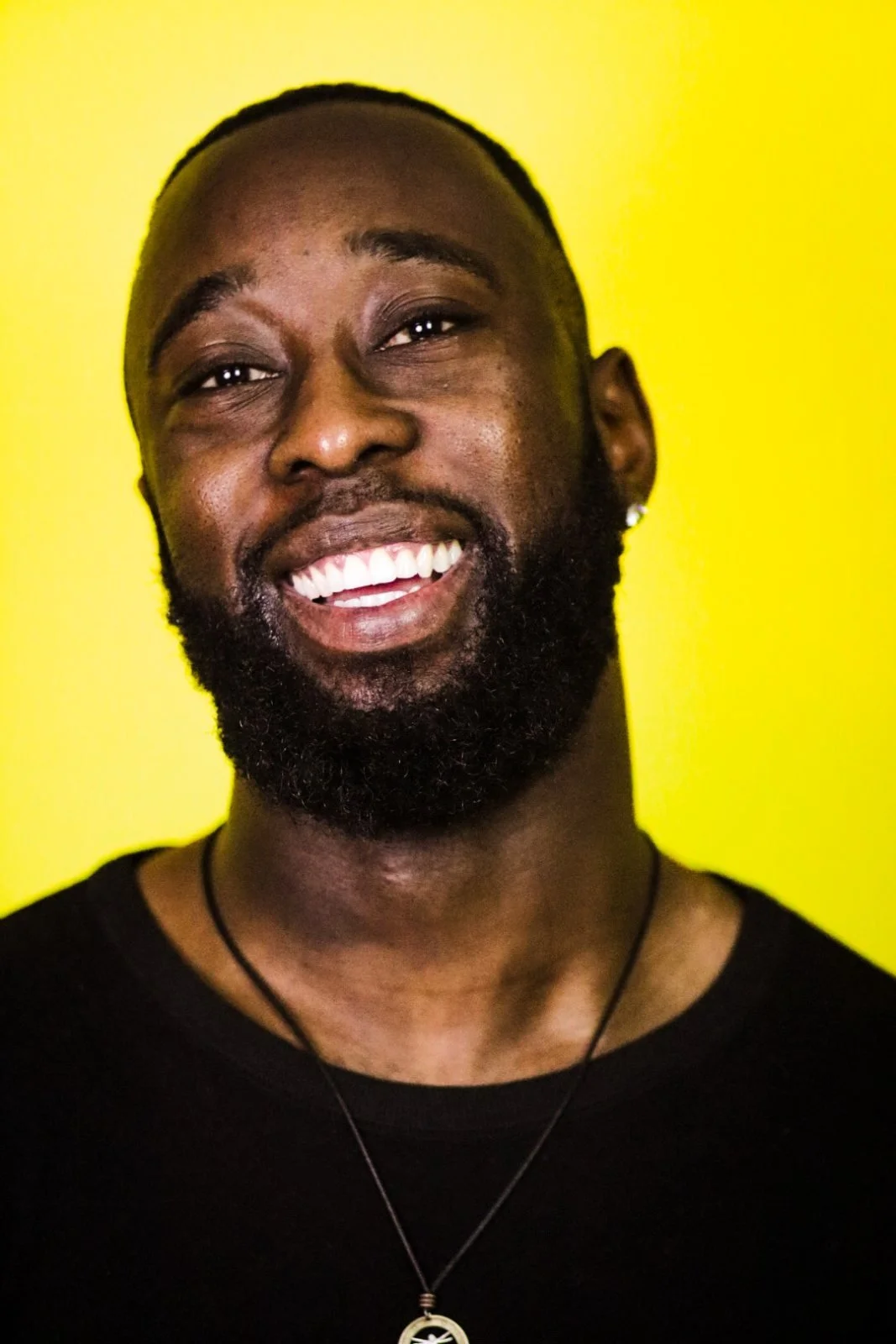 Close-up portrait of St. James Jackson laughing against a yellow background.