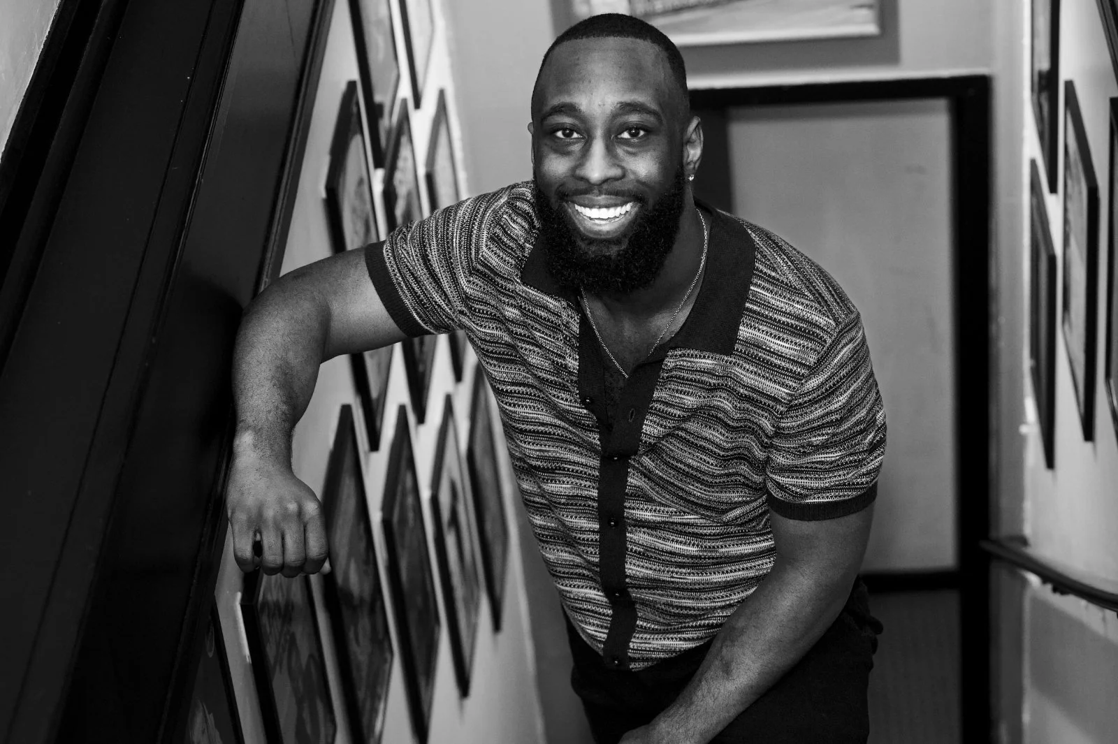 Black-and-white portrait of St. James Jackson smiling in a hallway lined with photographs.
