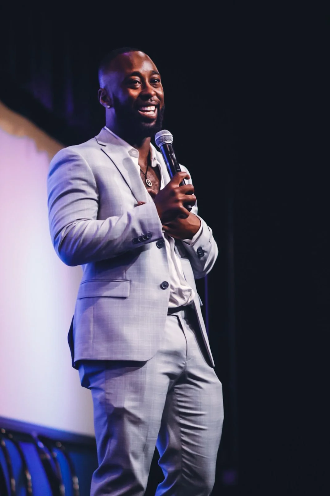 St. James Jackson smiling into a microphone while performing in a grey suit.