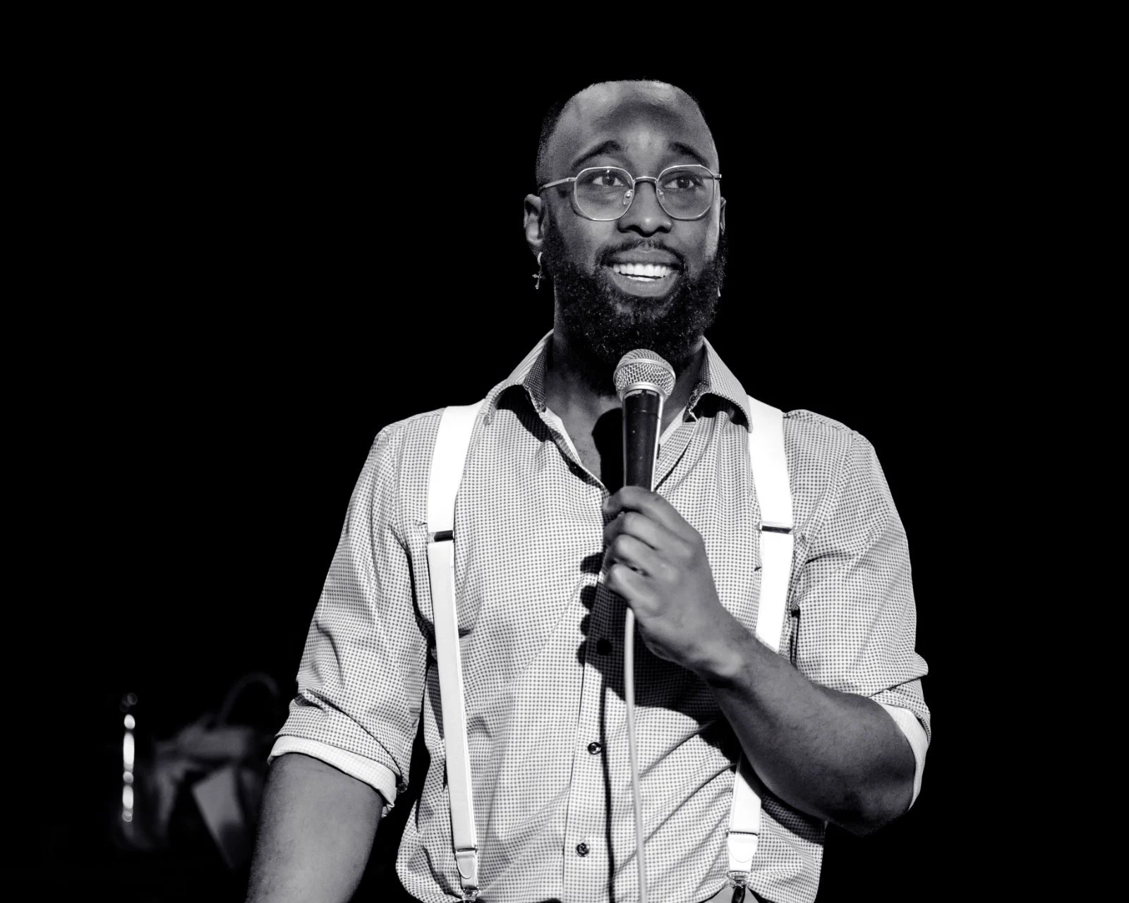 Black-and-white photo of St. James Jackson smiling with a microphone and wearing suspenders.