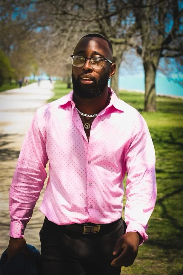 St. James Jackson wearing a pink shirt and glasses on a tree-lined lakefront path.
