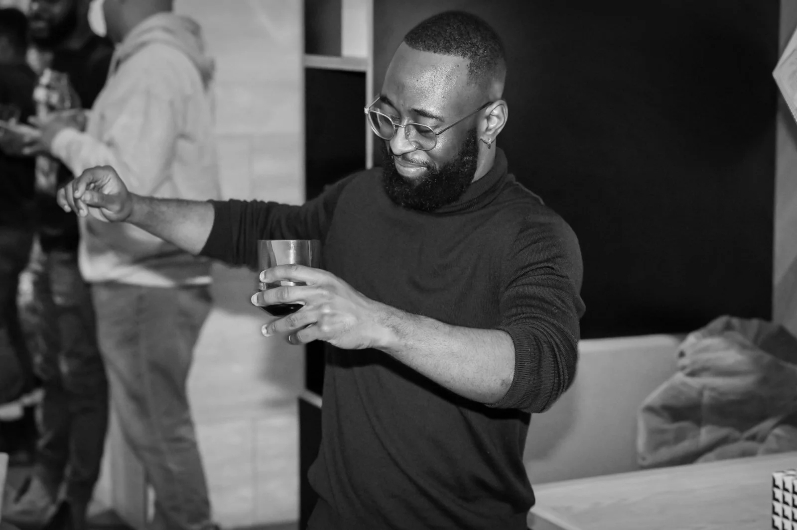 Black-and-white candid photo of St. James Jackson holding a wine glass and extending his arm.