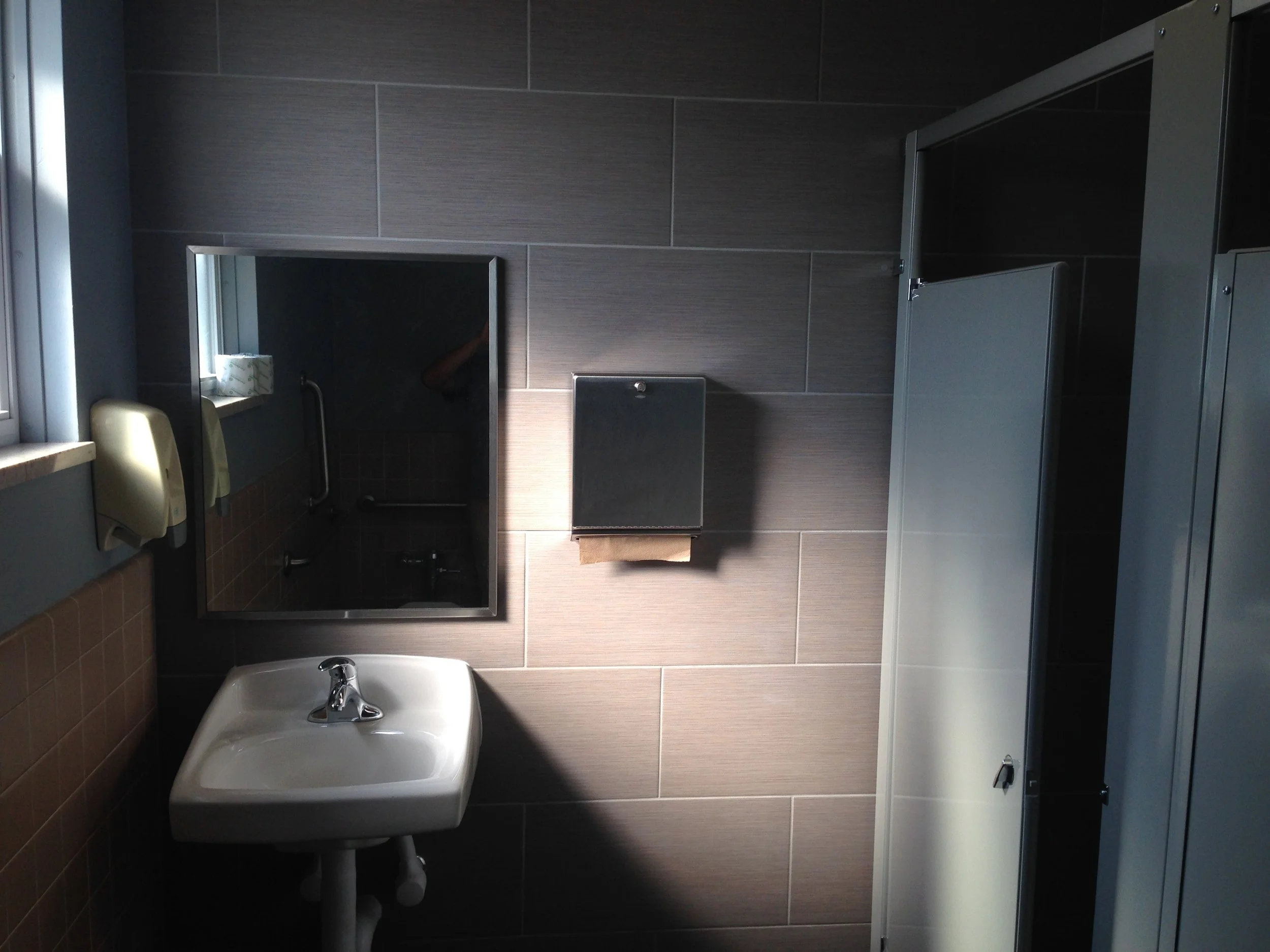 Renovated church restroom with updated tile, wall-mounted mirror, and modern fixtures.JPG