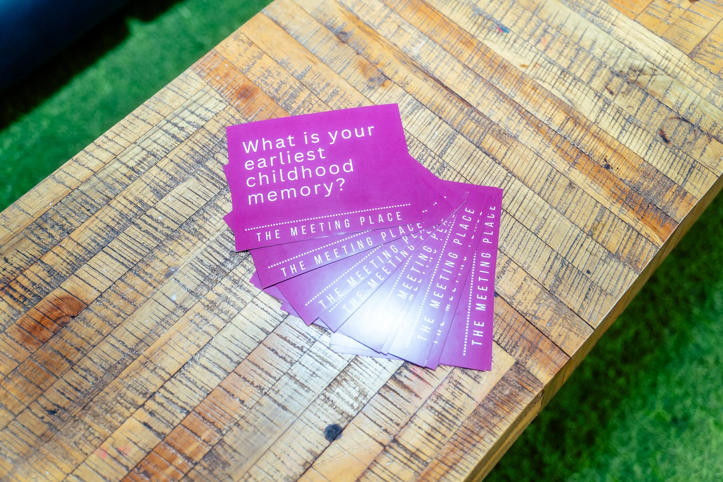 pile of purple card placed on top of wooden table with a question that asks "what is your earliest childhood memory? the meeting place"