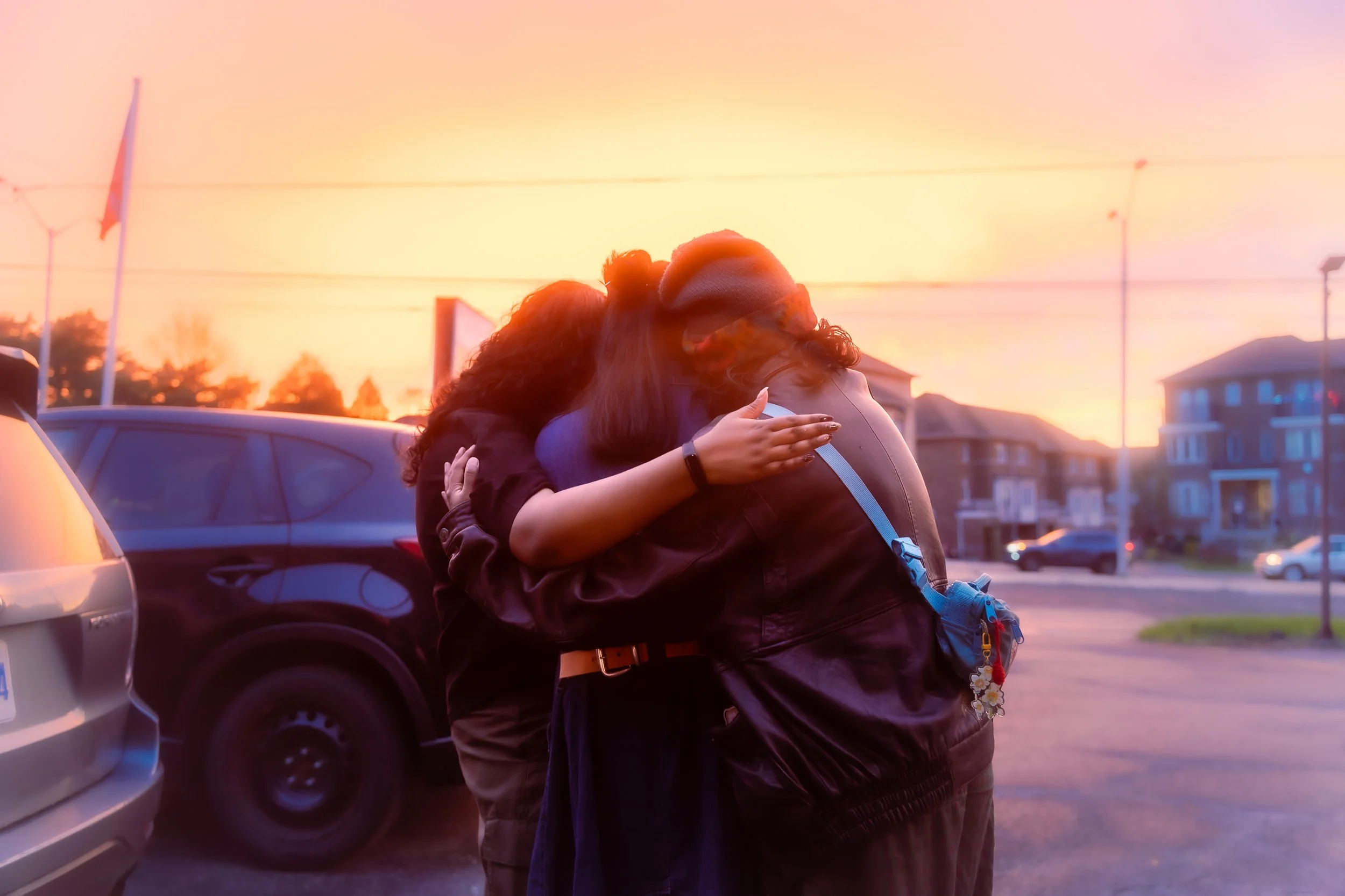 picture of Theyva, Daisy, and Sun (left to right) hugging each other in front of a sunset.