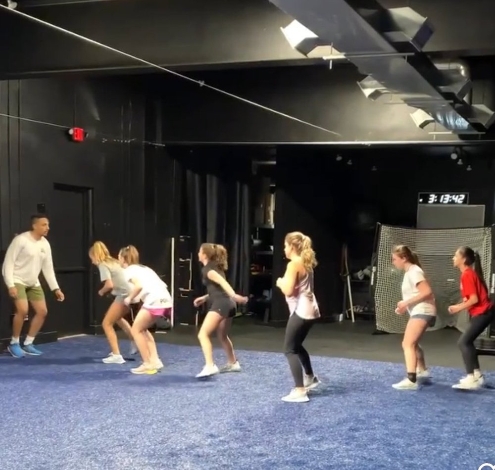 Athletes moving through an agility drill on the indoor turf while a Char Sports Performance coach watches their form
