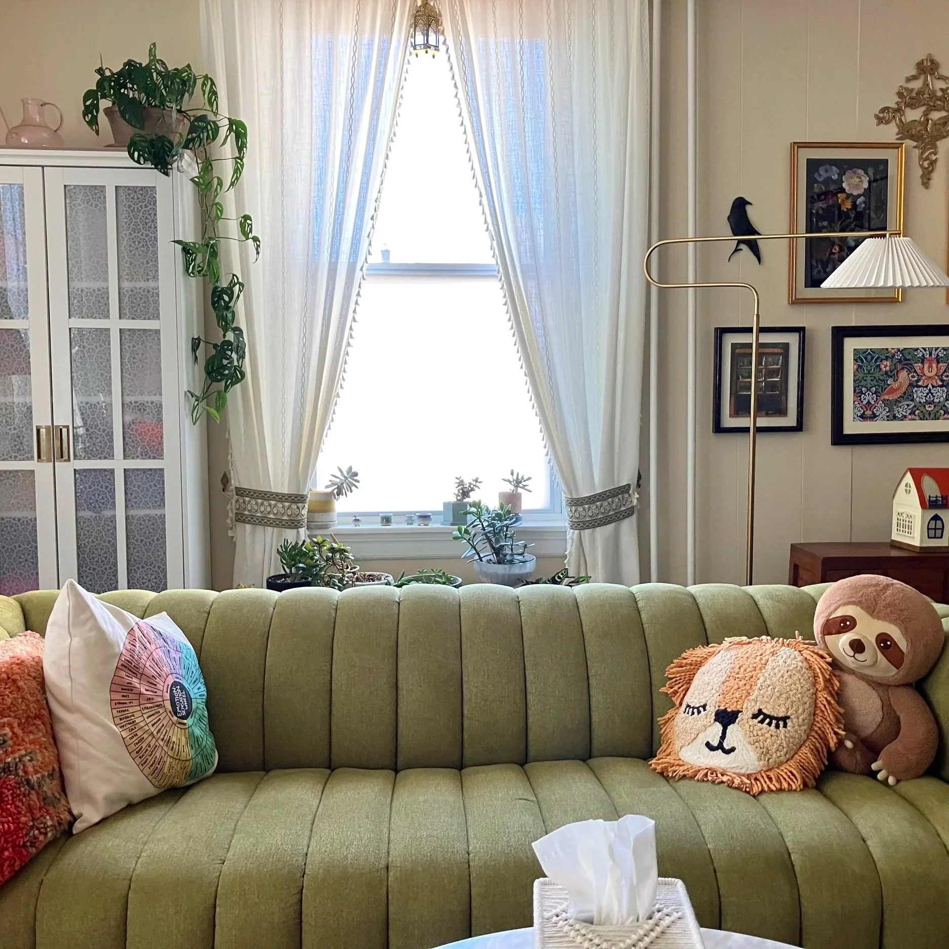 A photo of the green sofa at Oak Grove Counseling LLC in Havertown. The large windows let in natural light, while offering privacy in the space. Pillows, art and plants create an atmosphere of peace.