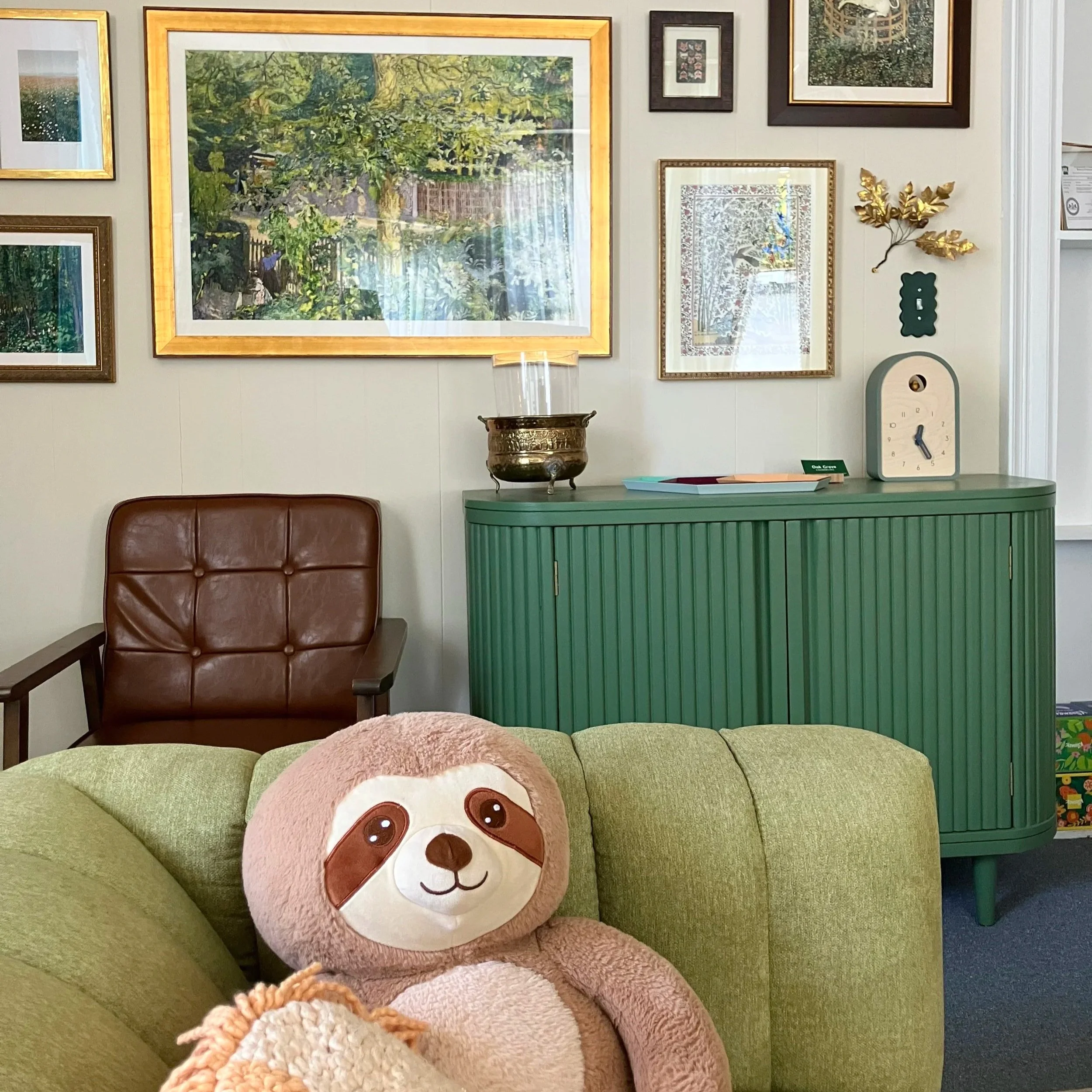 A photo of a weighted sloth toy, cuckoo clock, and art wall in the office of Oak Grove Counseling, LLC, where Meg Rogers, LMFT provides empirically supported EMDR therapy, play therapy, DBT therapy and talk therapy to address trauma, anxiety, and neu