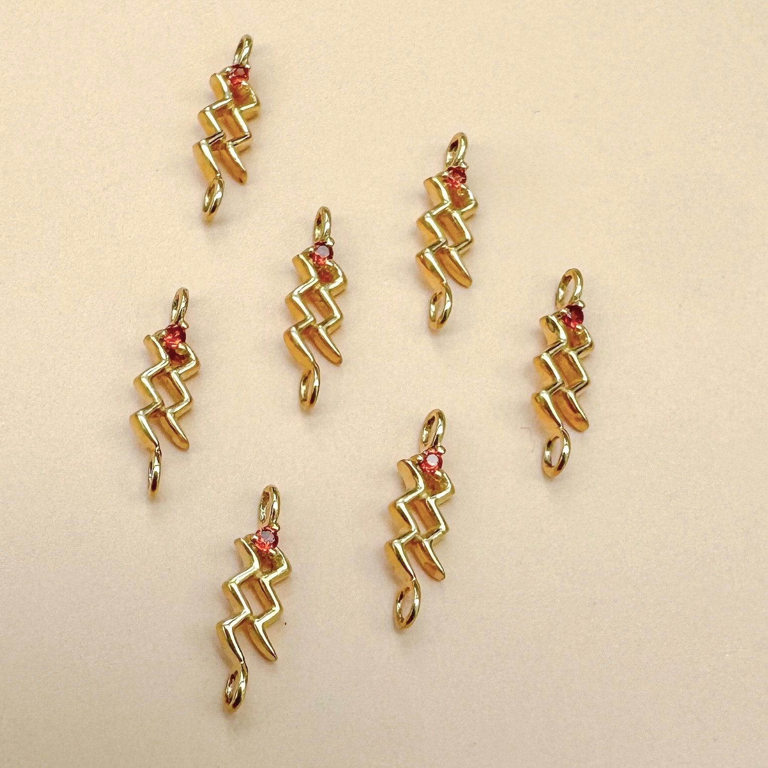 Aquarius zodiac charm in solid 14k gold with natural garnet birthstone. Permanent jewelry by The Sparkle Bar, Edmonton. Shop zodiac
