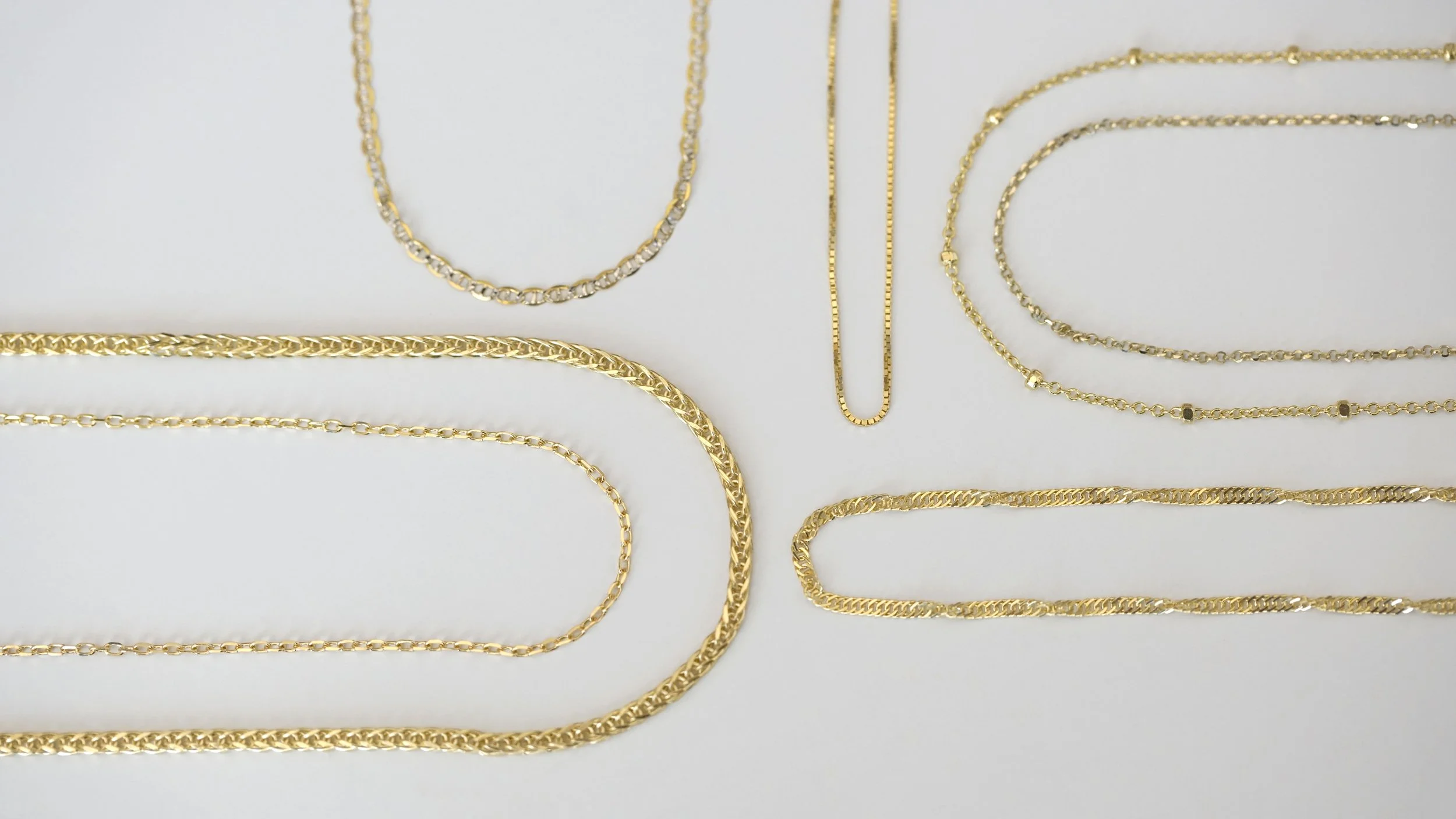 Gold chains of various styles and lengths laid out on a white surface.