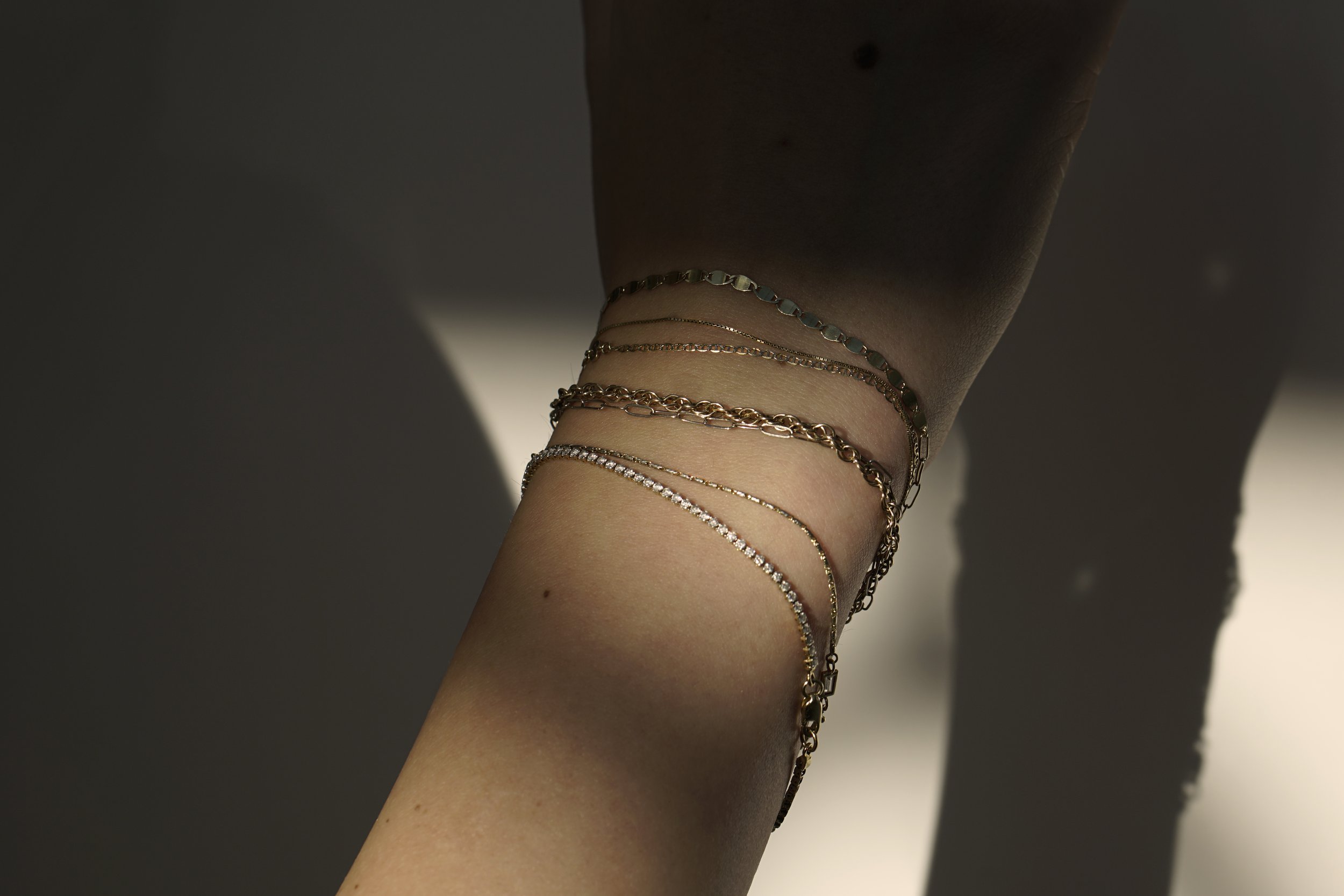 A stack of classic solid 14k gold bracelets featuring a 1.5mm diamond tennis bracelet from The Sparkle Bar in Edmonton