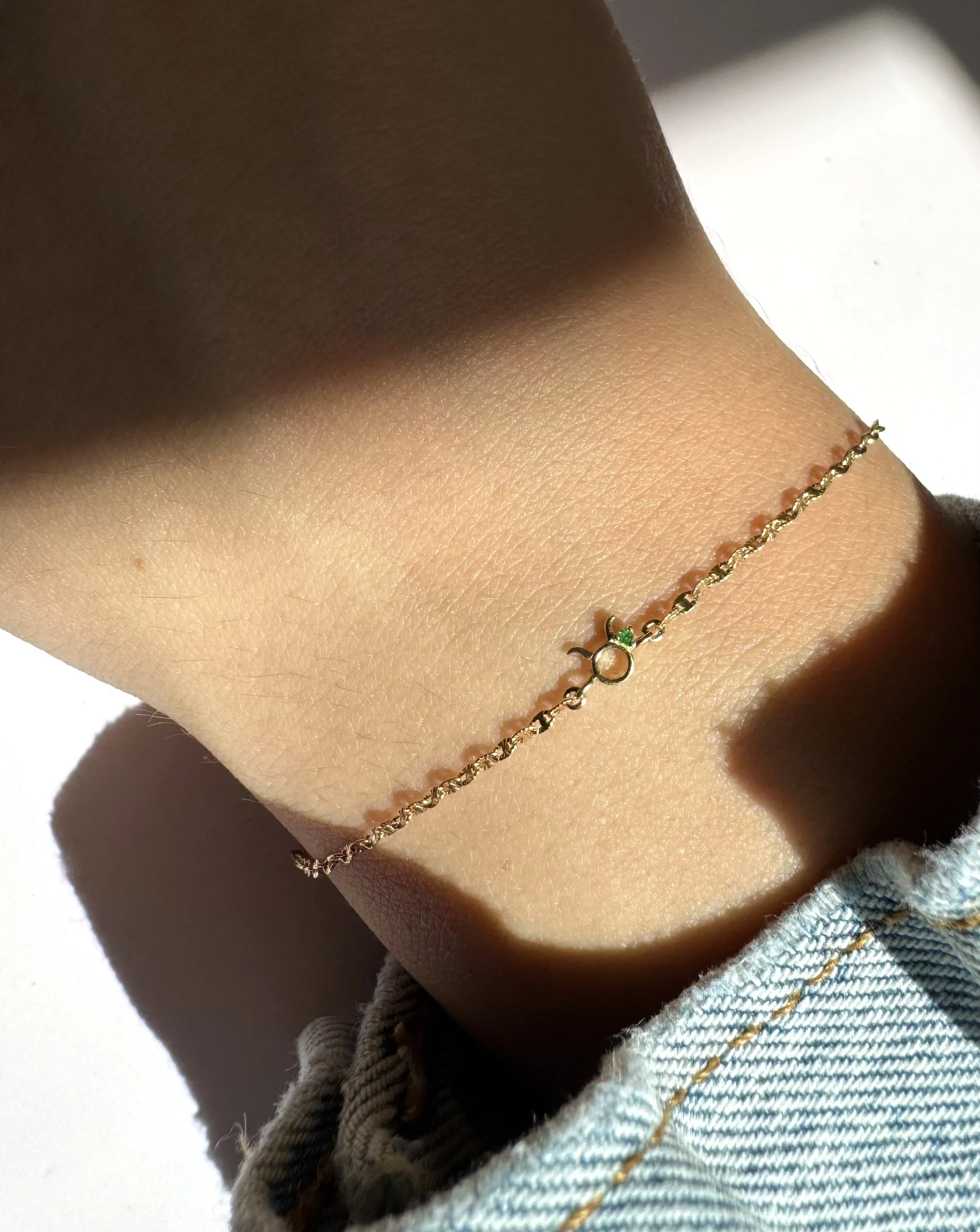 Taurus zodiac bracelet in solid 14k gold shown on model. Natural emerald birthstone. From The Sparkle Bar in Edmonton. Shop permanent jewelry online or book the studio.