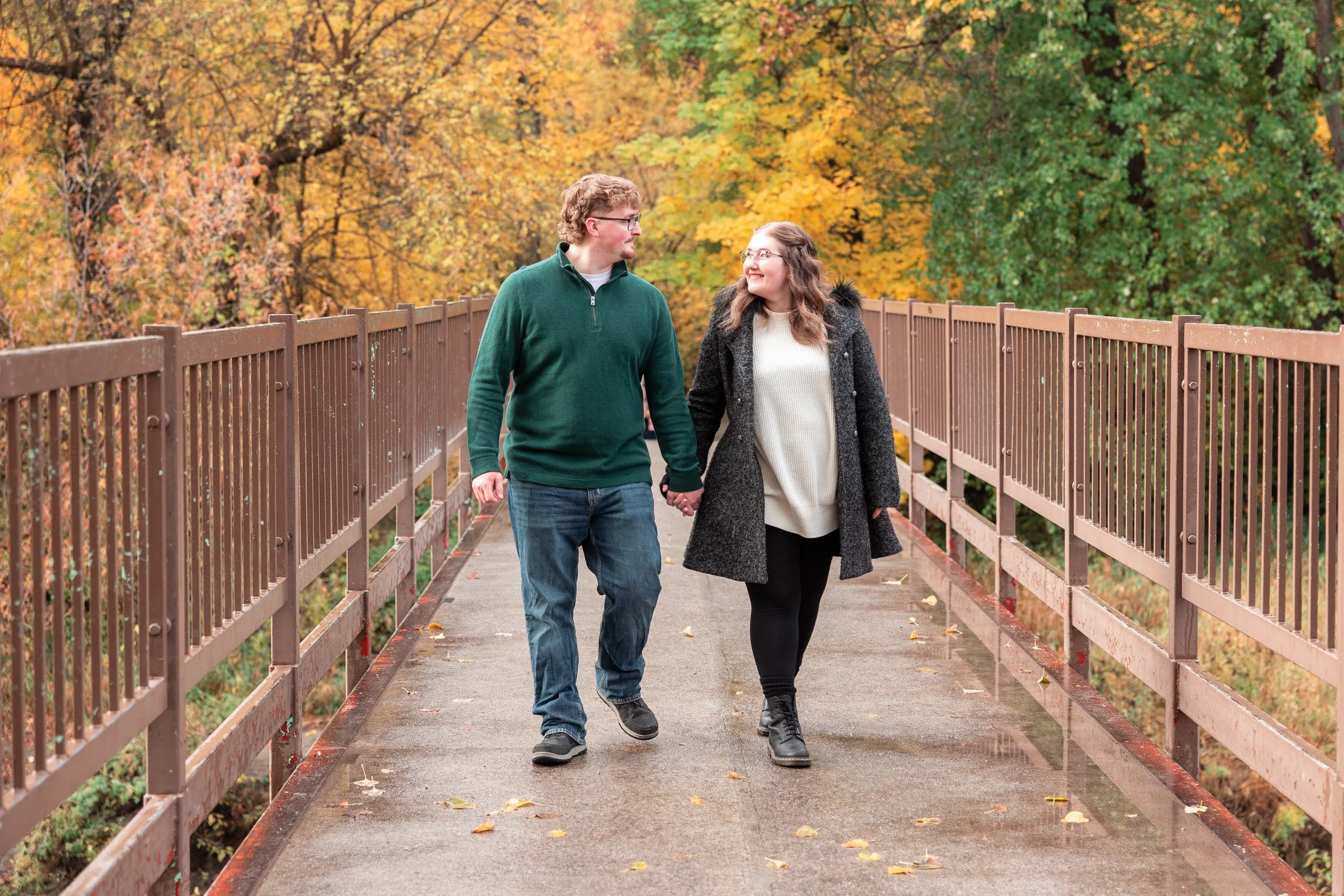 Couple holding hands looking at each other smiling walking over Leavenworth bridge with fall colors in background