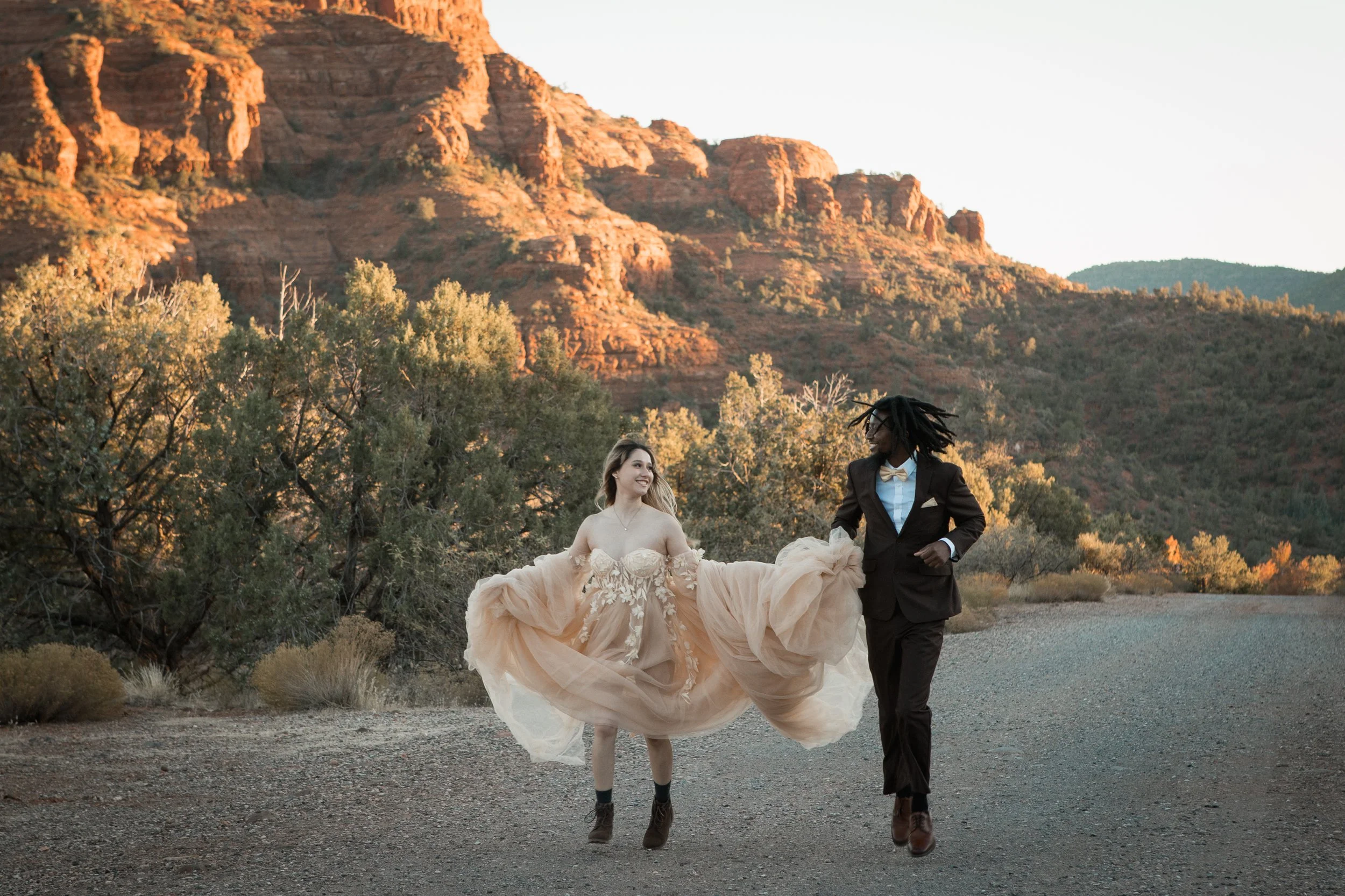 Sedona engagement Couple in formal wear laughing and running in Sedona with red rock in background