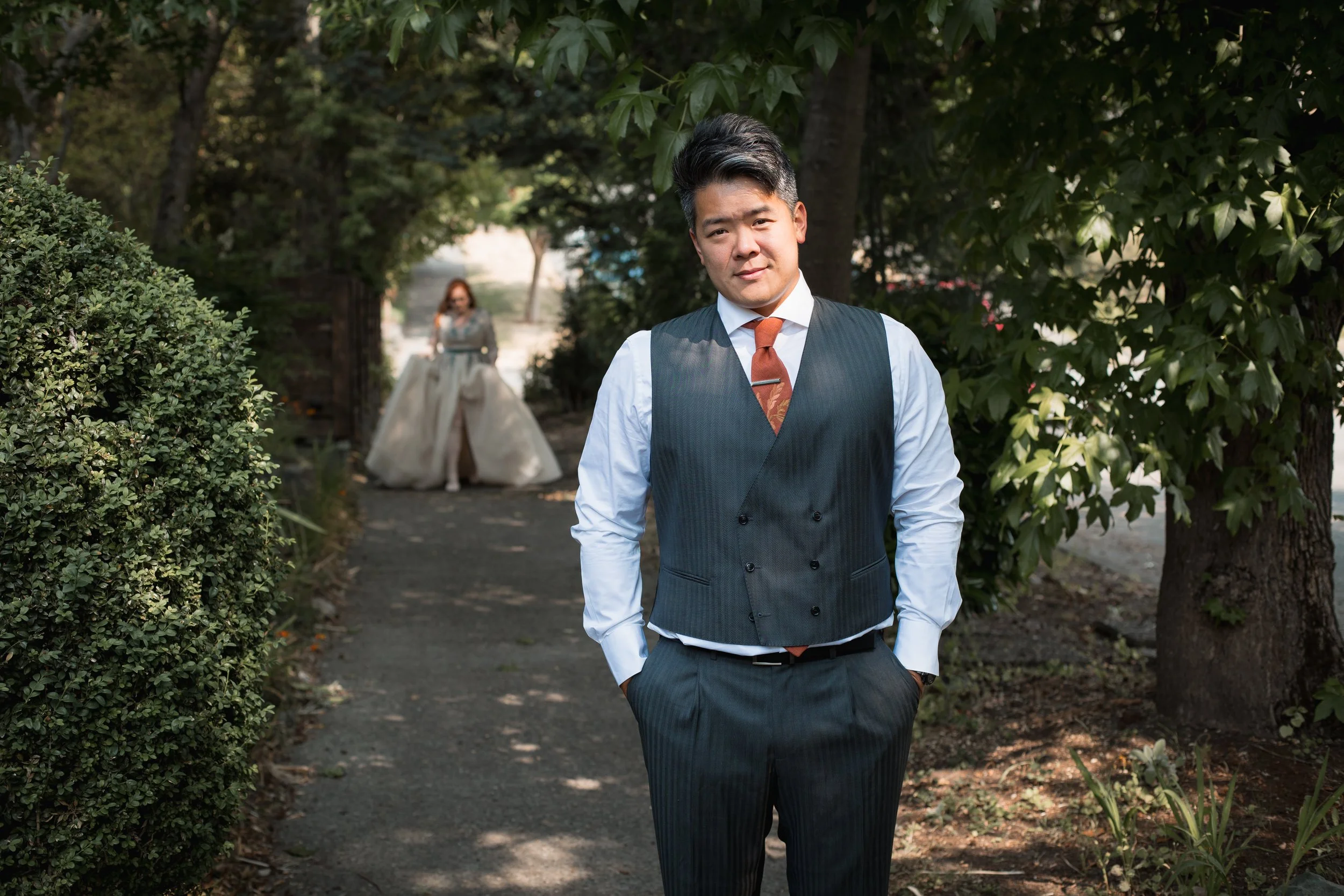 Groom facing camera while bride walks up behind him on a lush Seattle walkway