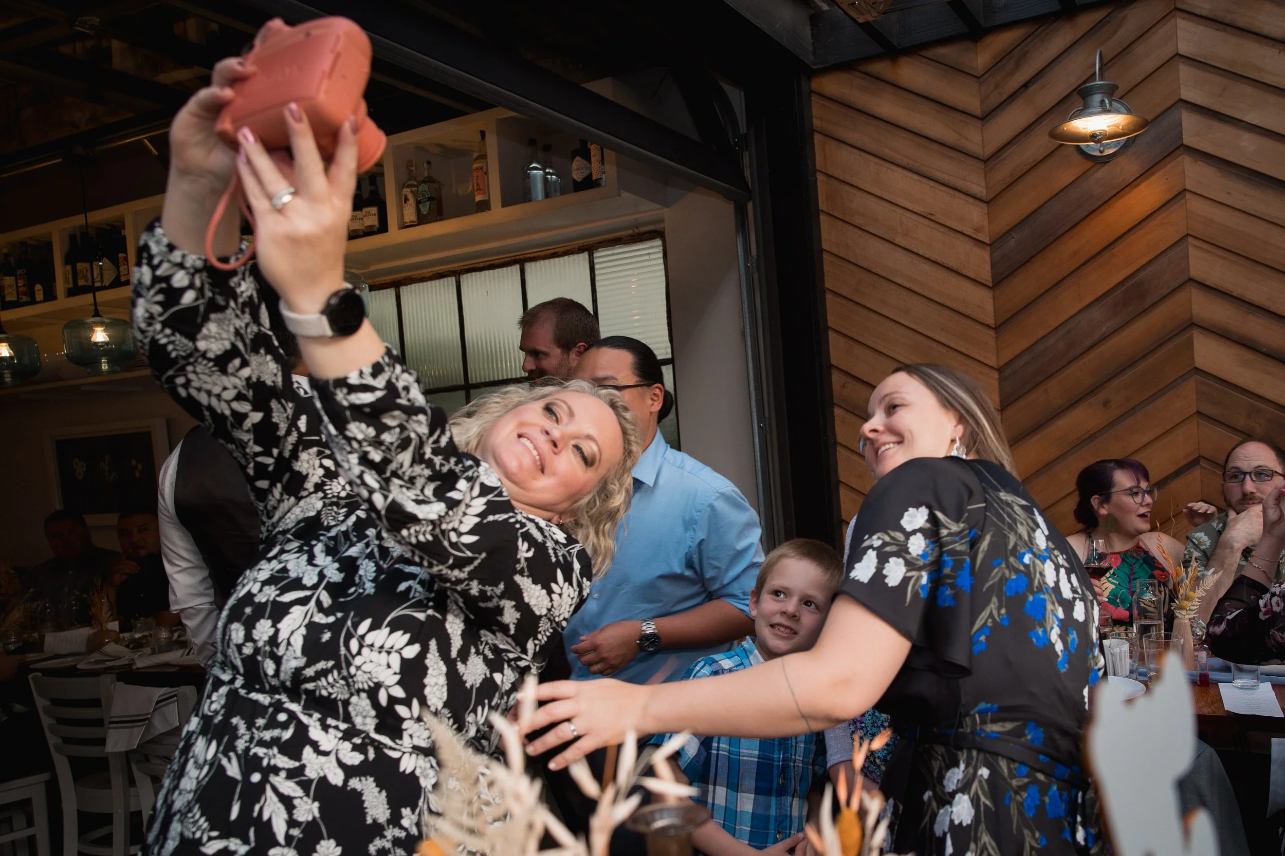 A group of people taking a selfie at a social gathering in a restaurant with wooden walls and dim lighting.