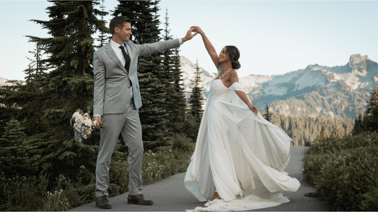 elopement bride and groom dancing in the mountains she has a long flowy dress and he is wearing a gray suit holding her bouquet