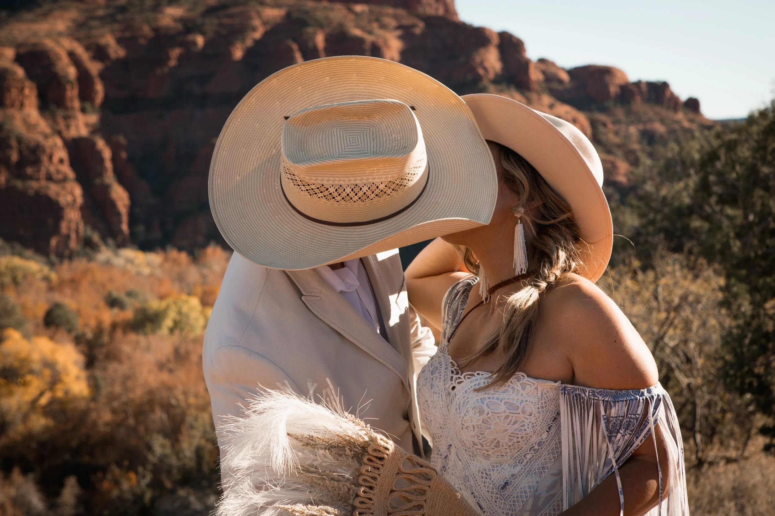 Western couple kissing with groom's hat covering both of their faces in the landscape of Sedona red rocks