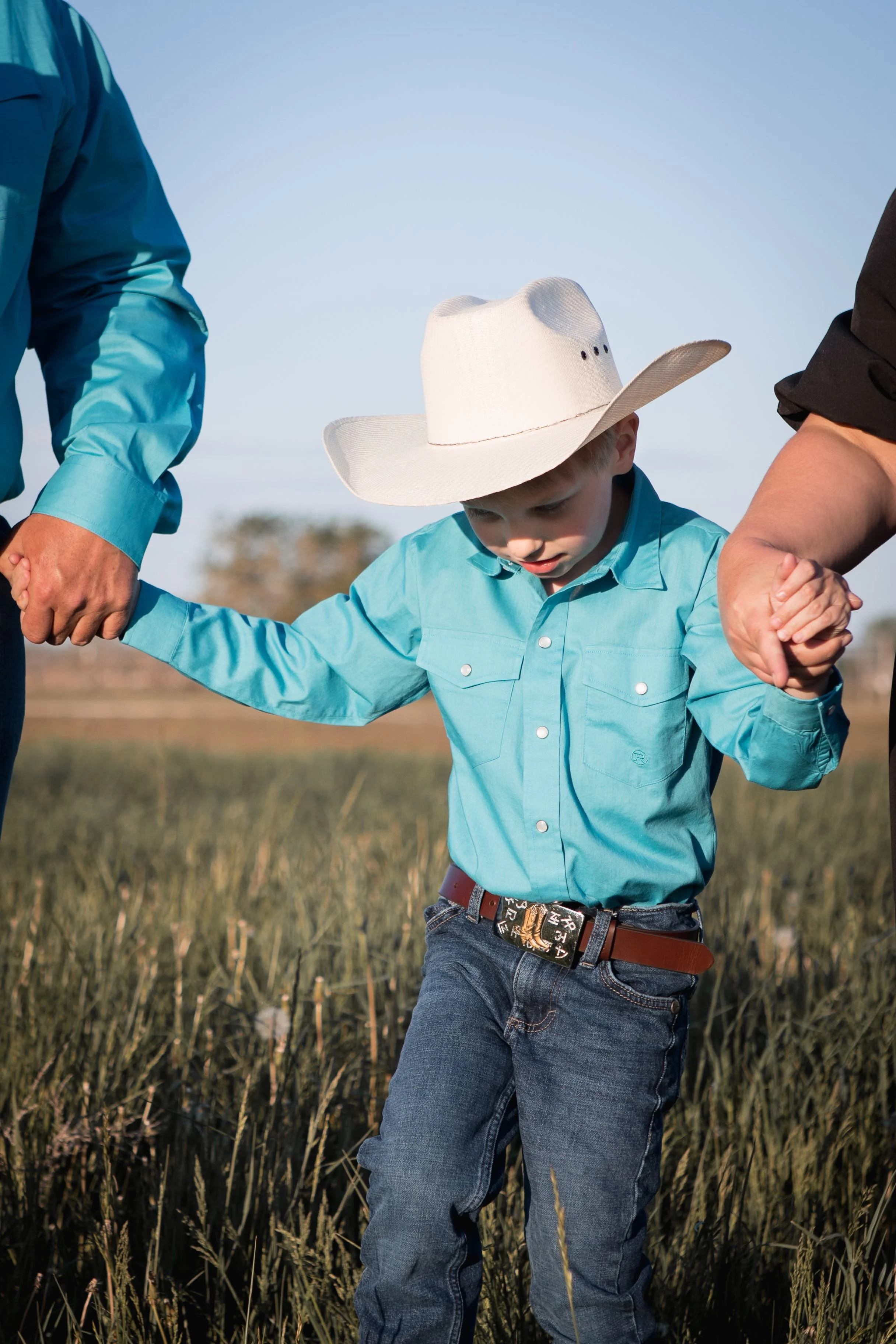 western style family holding sons hands and walking in the tall grass for family photos at their ranch