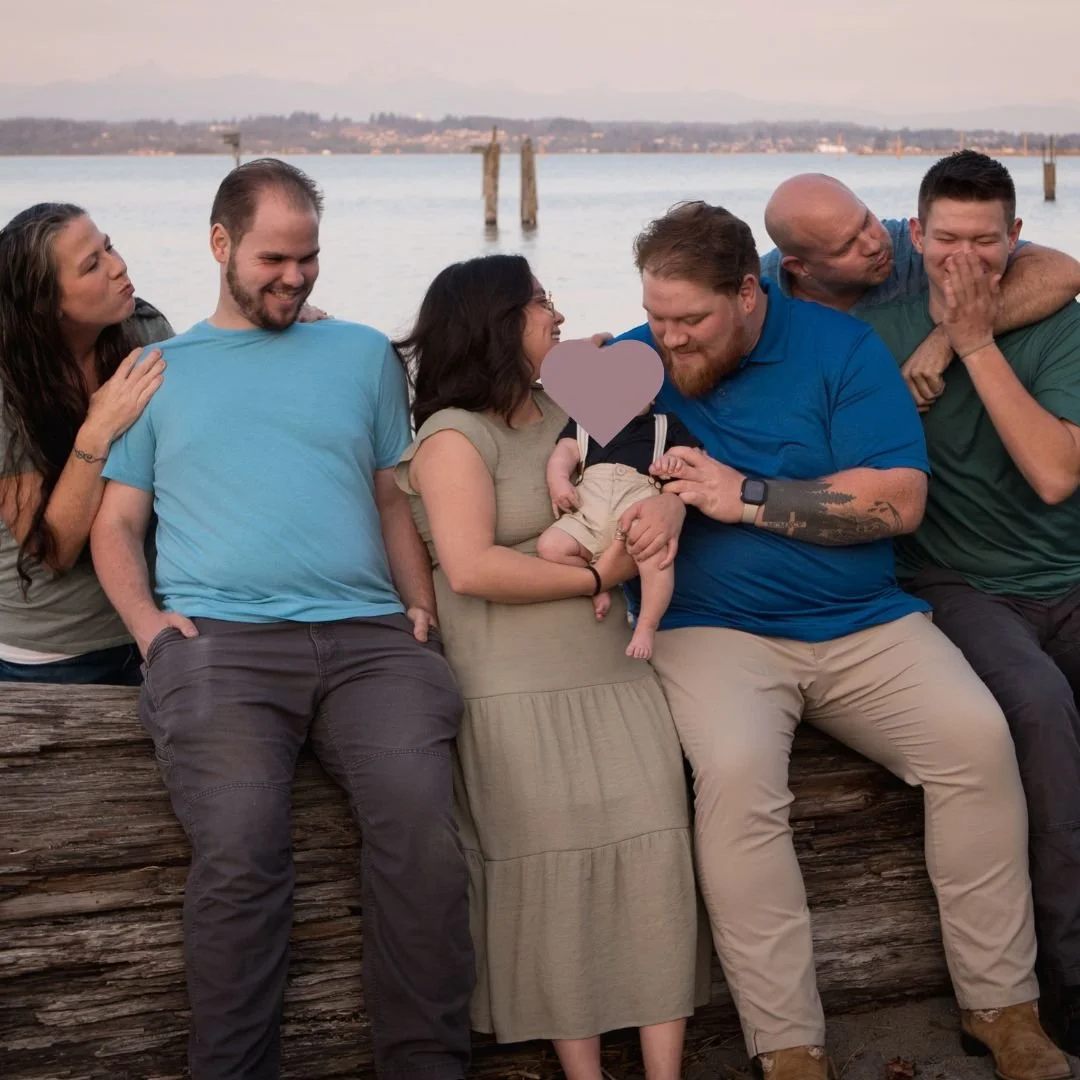 Camano island family sitting on a log at the water and making funny faces at each other for family photos