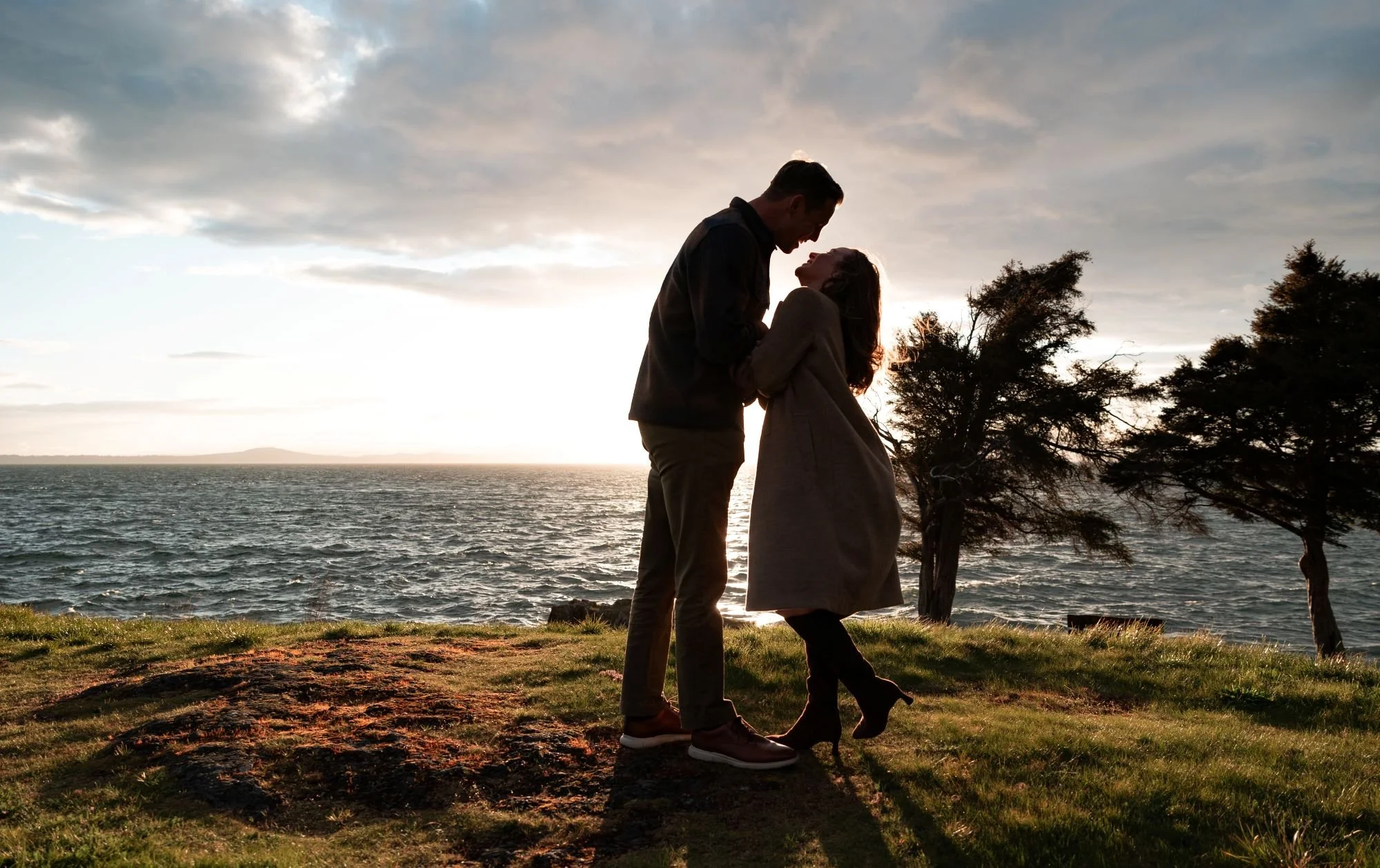 San juan Island couple embracing at San Juan County campground with water and tree in background at sunset with Olympic mountains in the distance