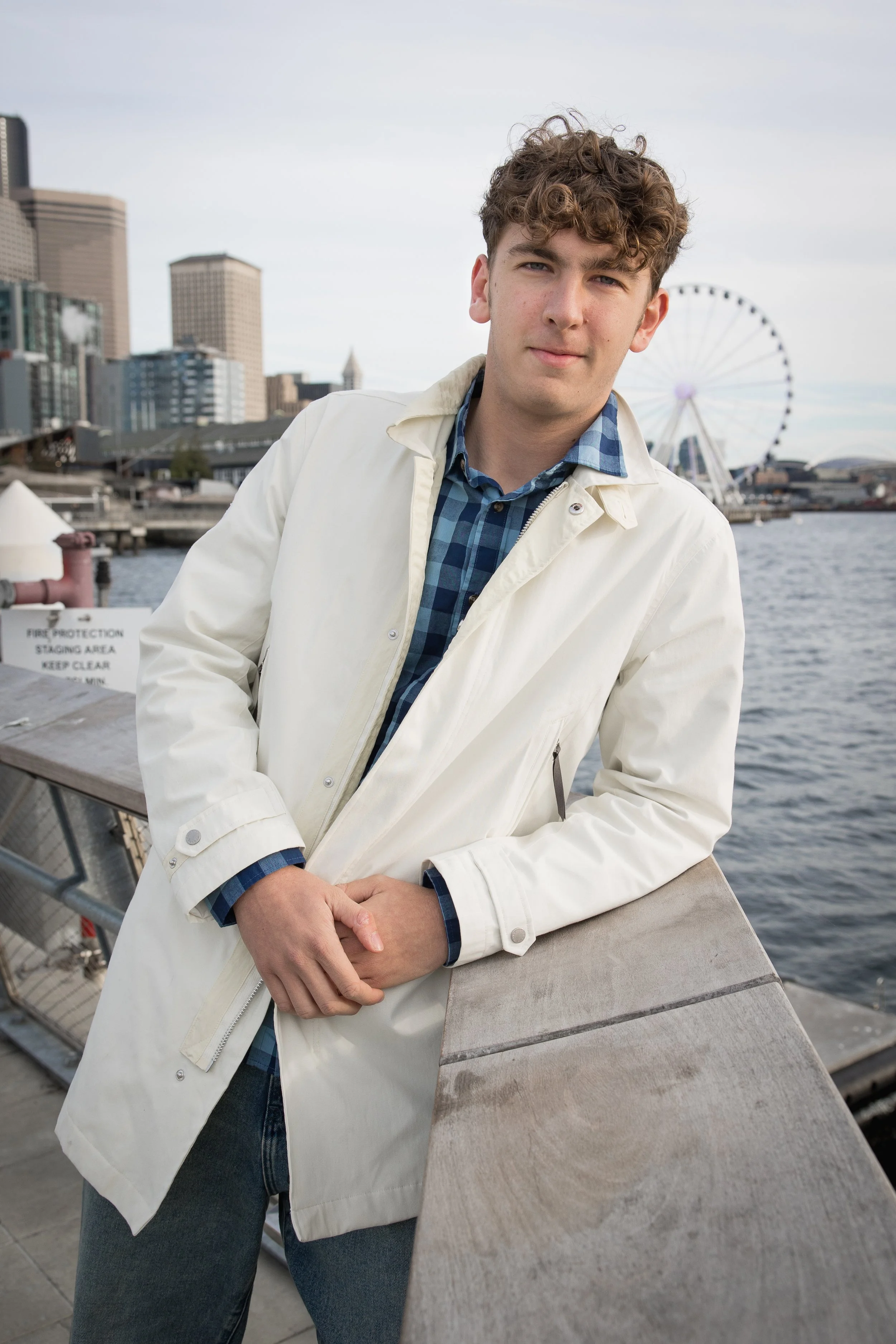 Oasis themed High school senior guy shoot at Seattle waterfront, him leaning towards the water looking at camera