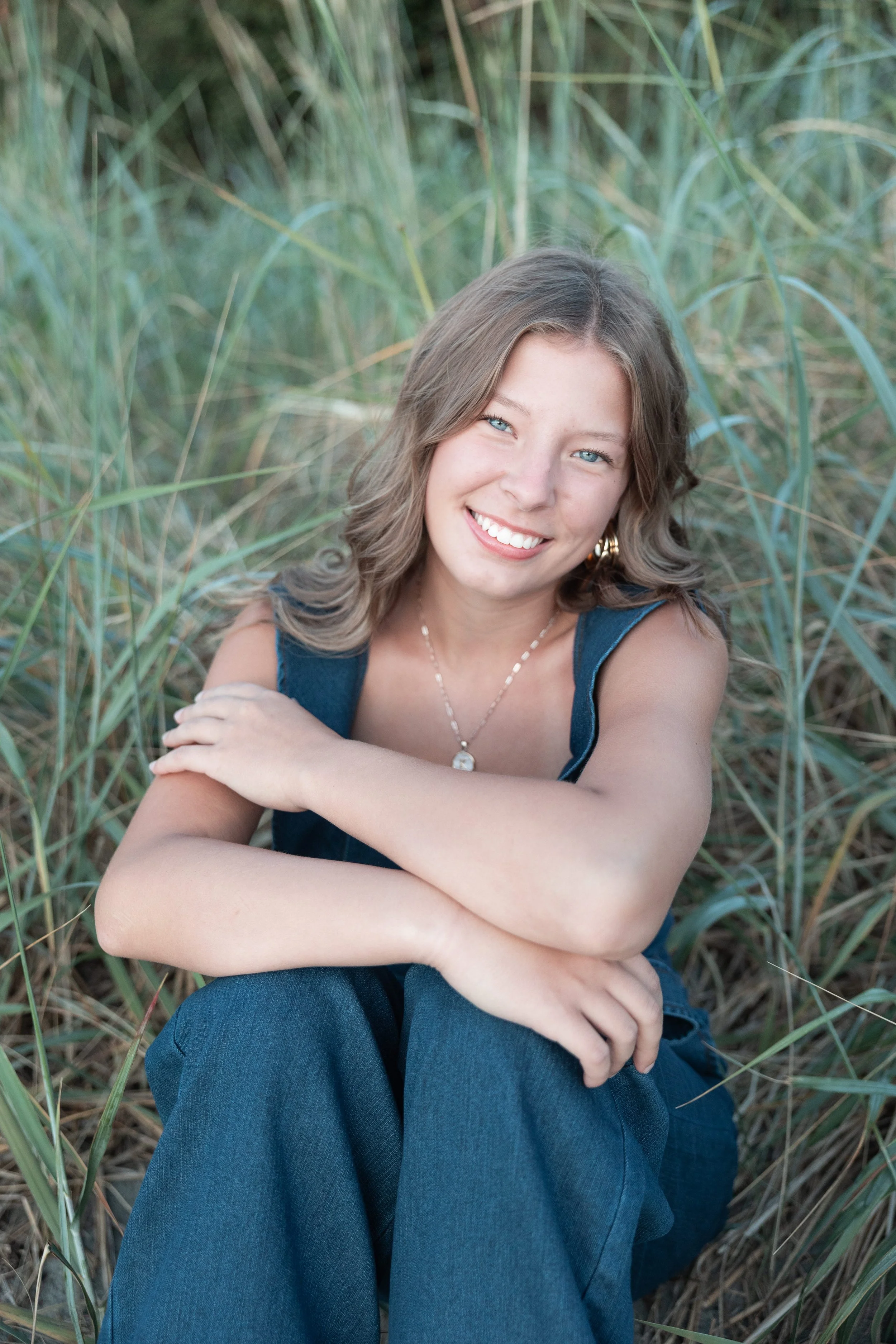 High school girl sitting in tall grass at the waterfront in Mukilteo