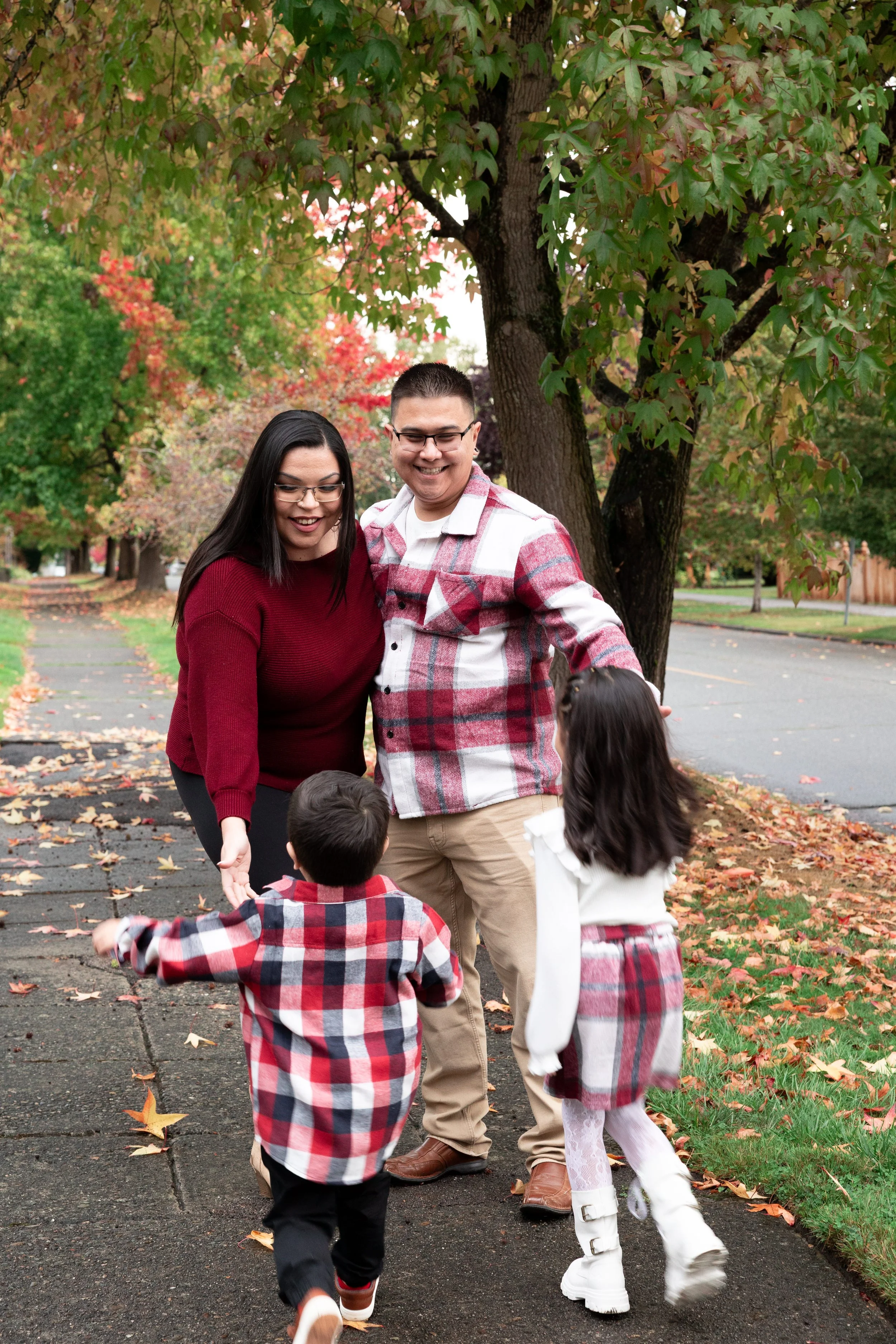 family of four, mom and dad have open arms welcoming their children that are running towards them under a maple tree in the fall