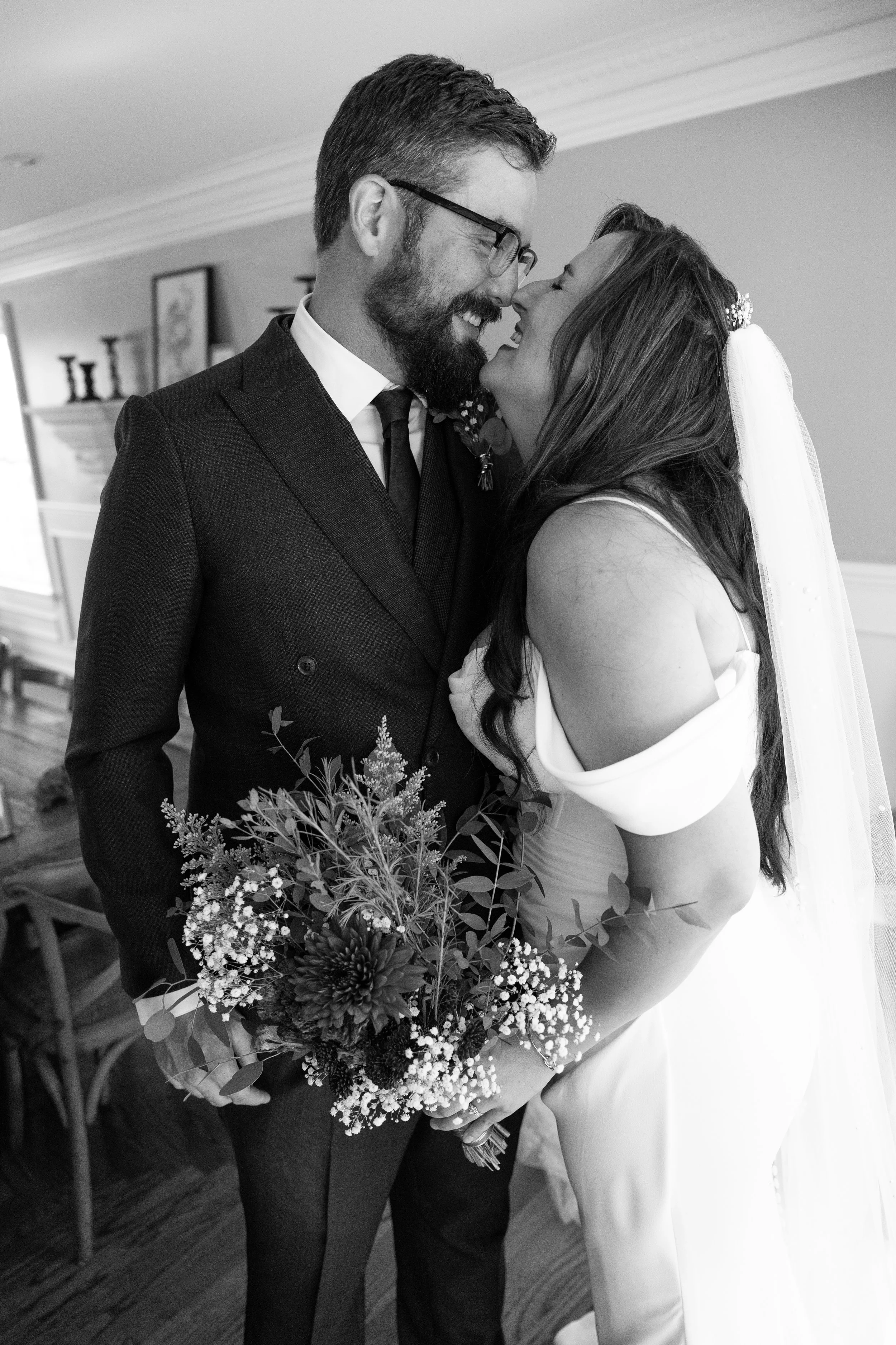 Black and white photo of a bride and groom in wedding attire, smiling and close together indoors.
