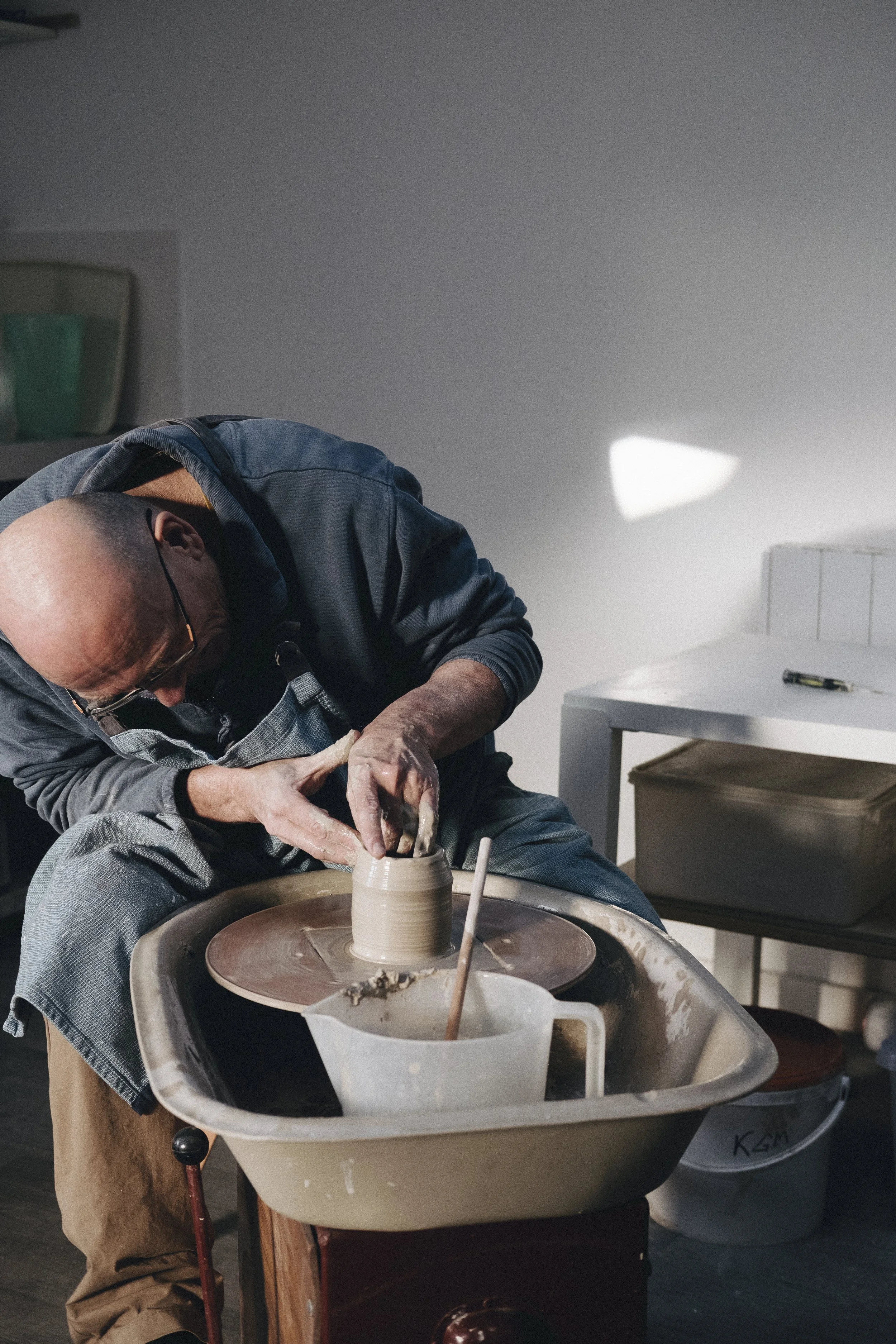 Potter throwing a pot on the wheel. Apron and hands are messy with clay