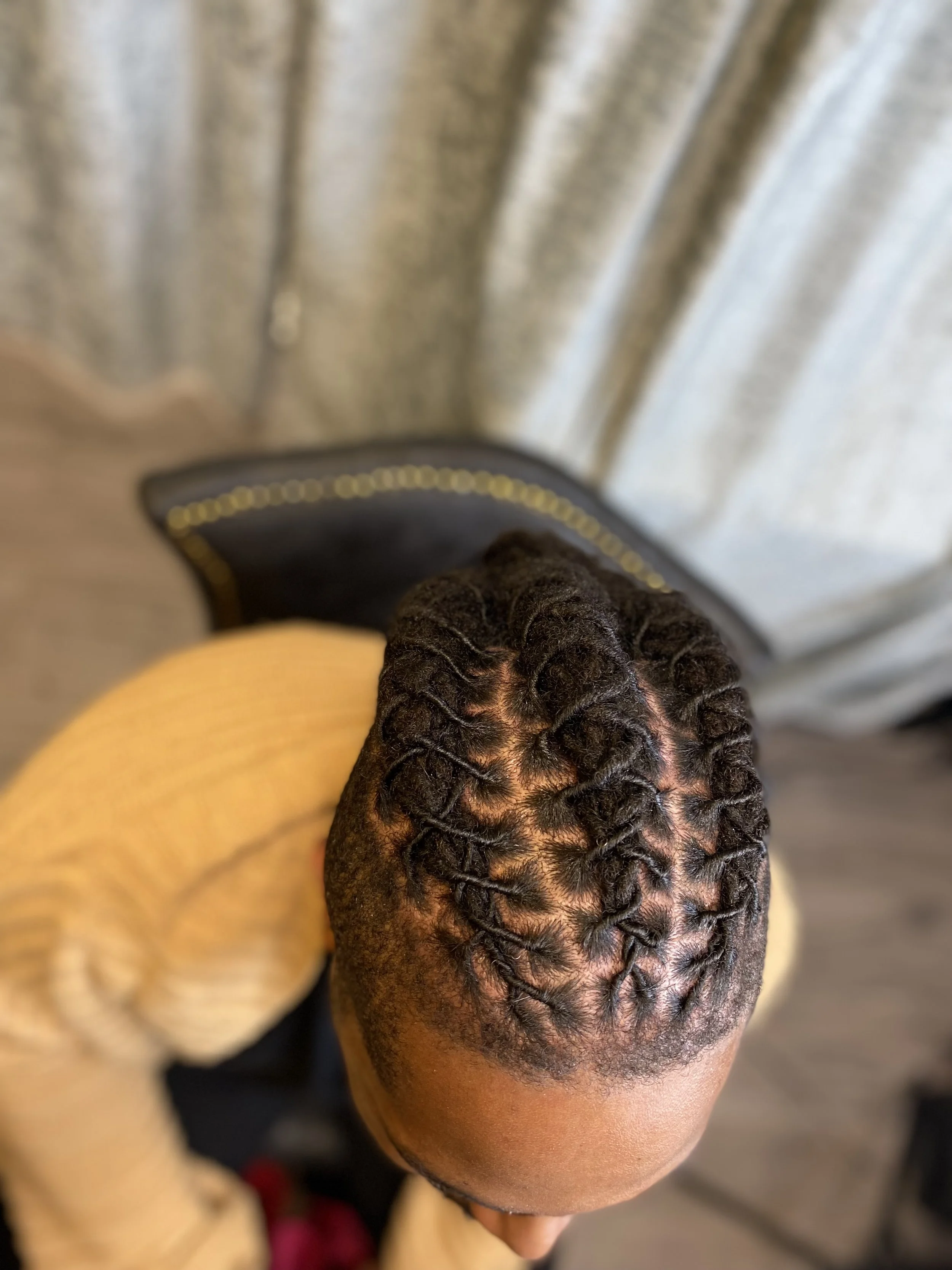 Top view of a person with freshly twisted hair styles in cornrows, wearing a yellow long-sleeve shirt, sitting on a chair.