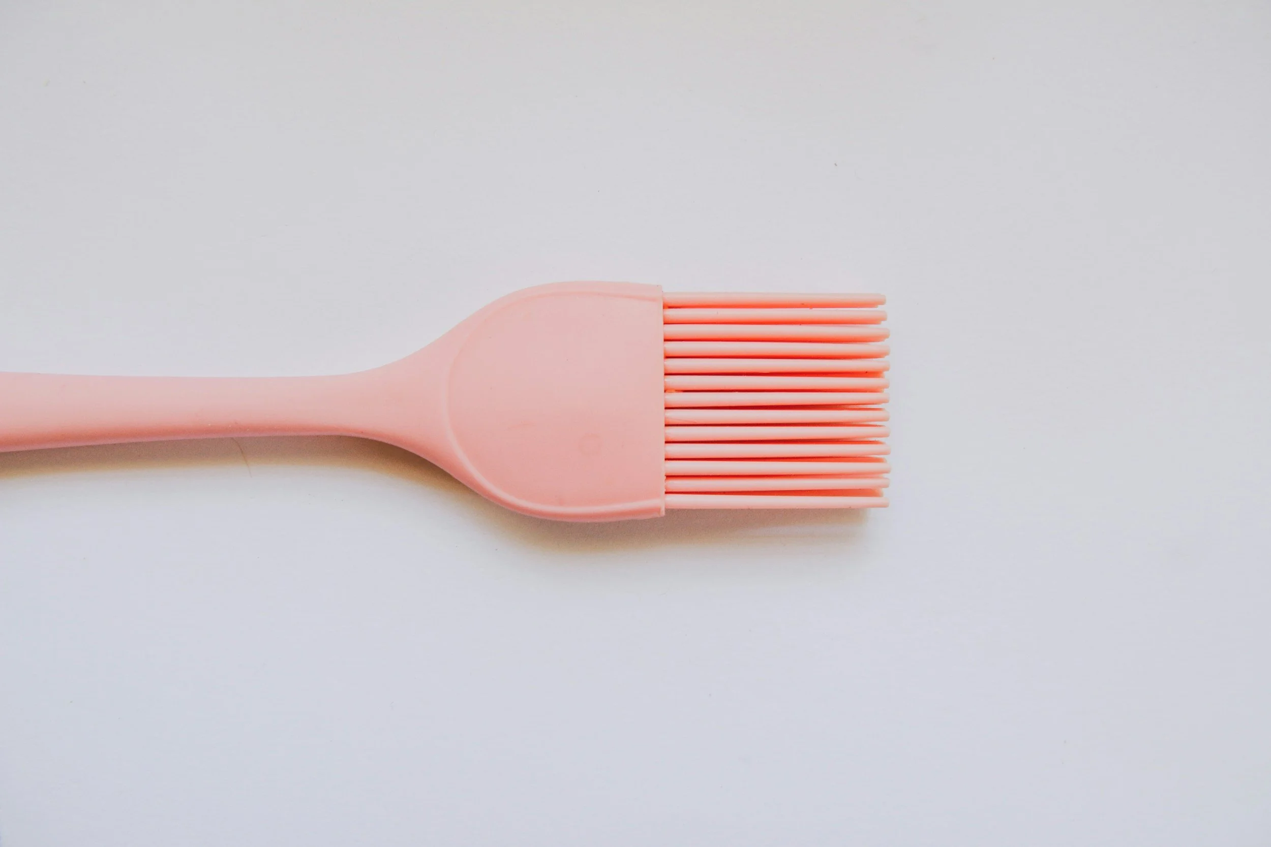 A pink silicone face brush with a flat handle and a rectangular brush head with soft bristles, on a white background.