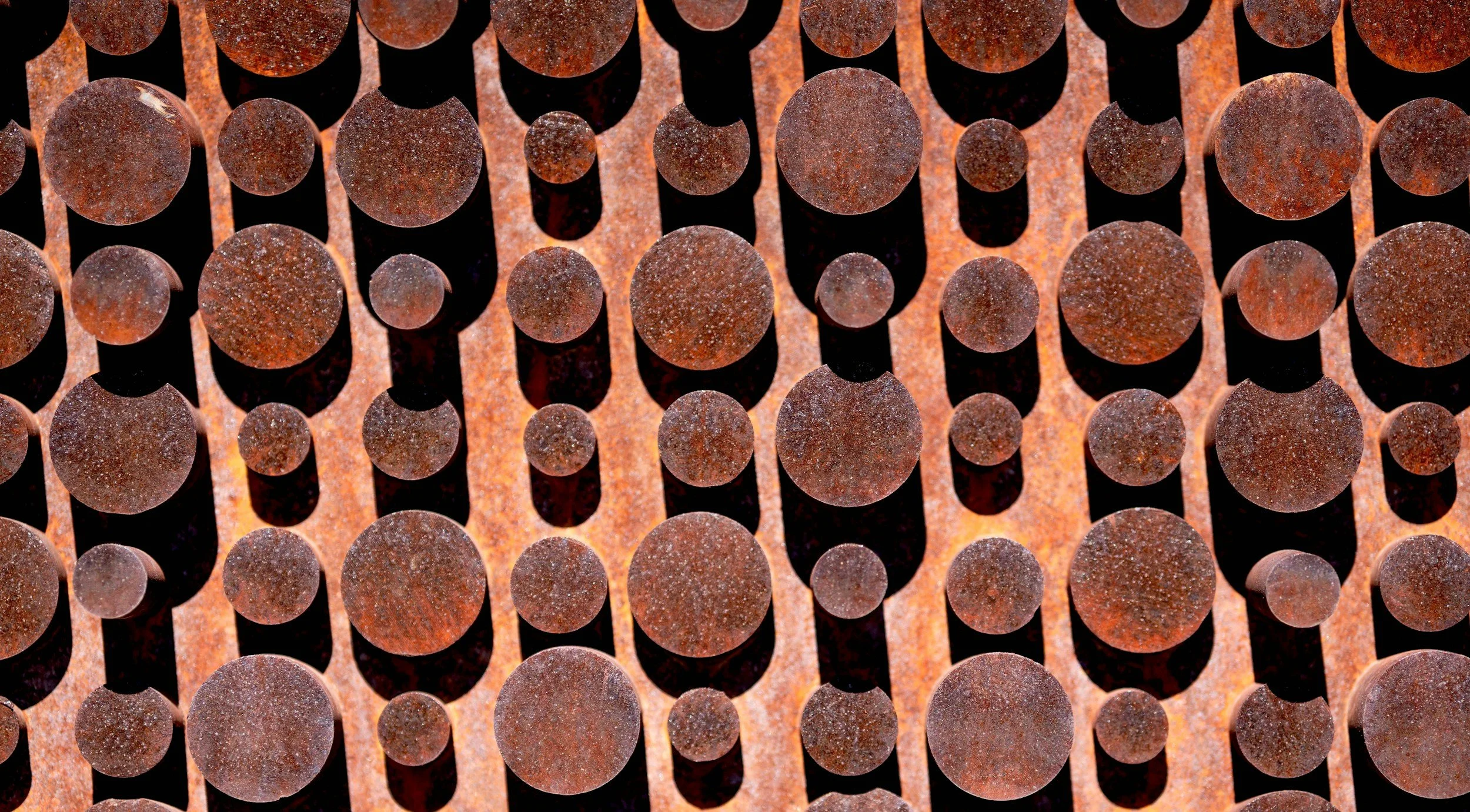 Close-up of rusty metal pipes arranged vertically, with shadows cast between them.