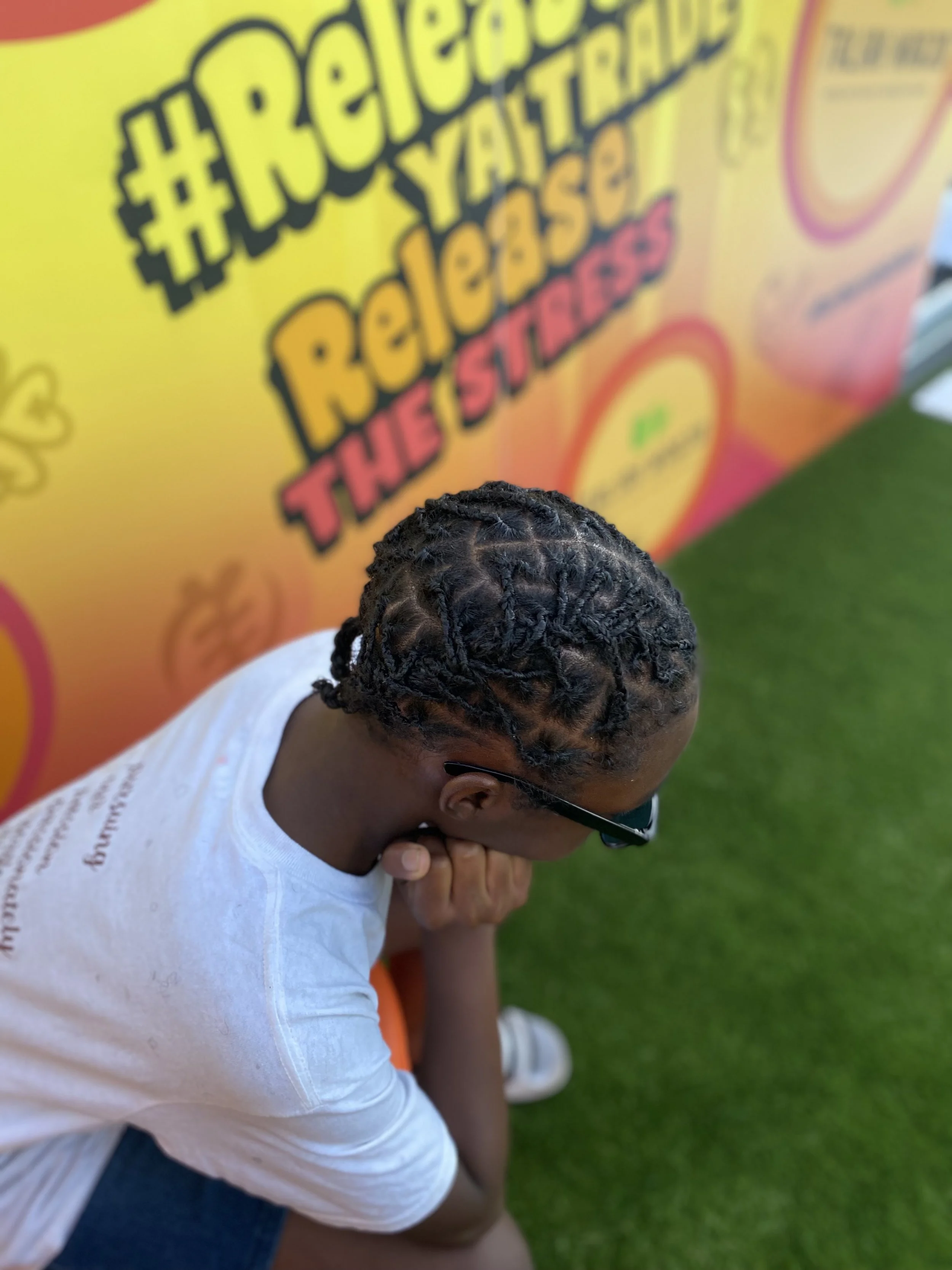 A person with braids and sunglasses sitting against a colorful background with the hashtag '#ReleasetheStress' and words 'Relaxation' and 'The Escape.'