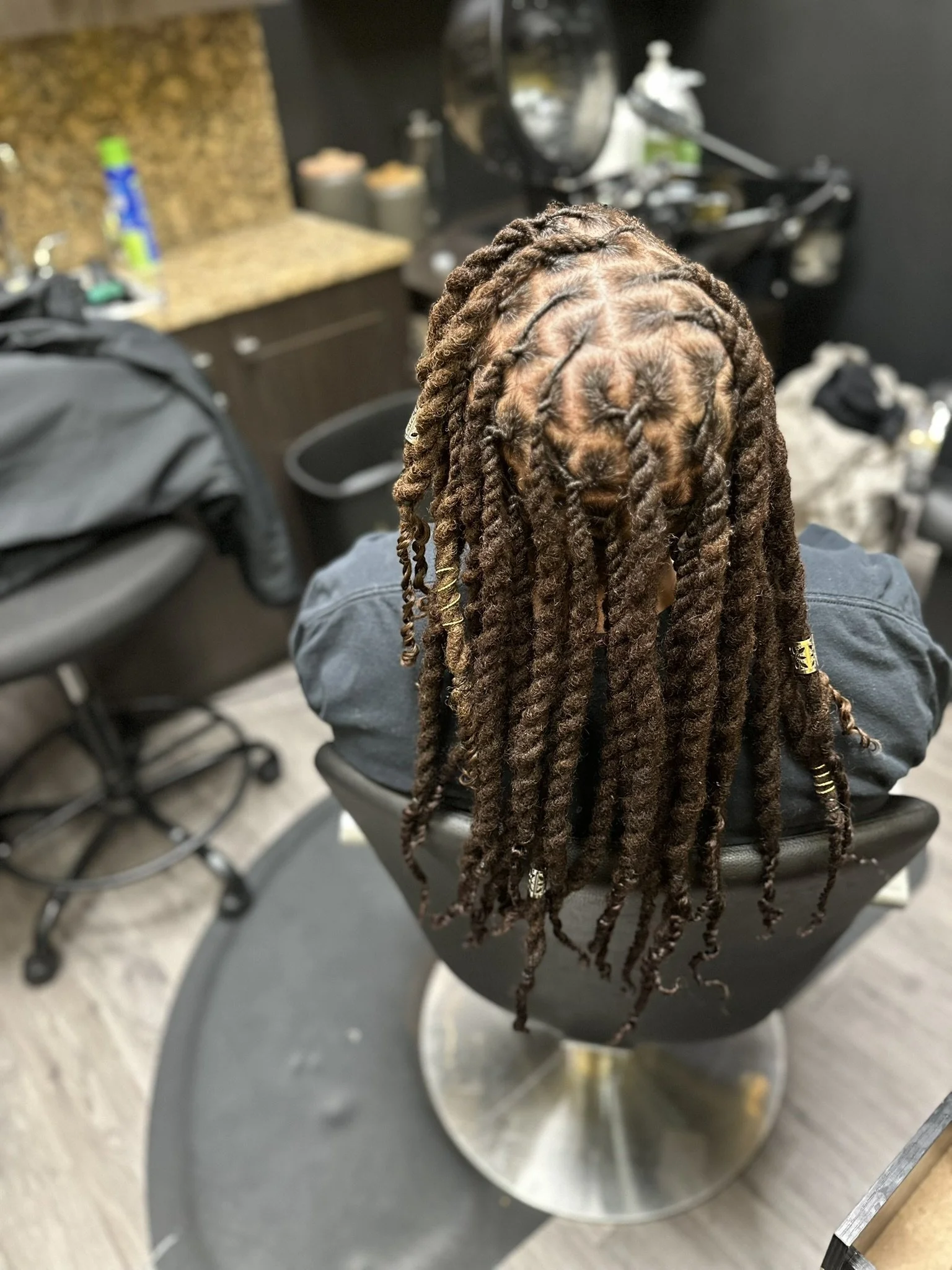 A person with dreadlocks sitting in a salon chair, viewed from above.