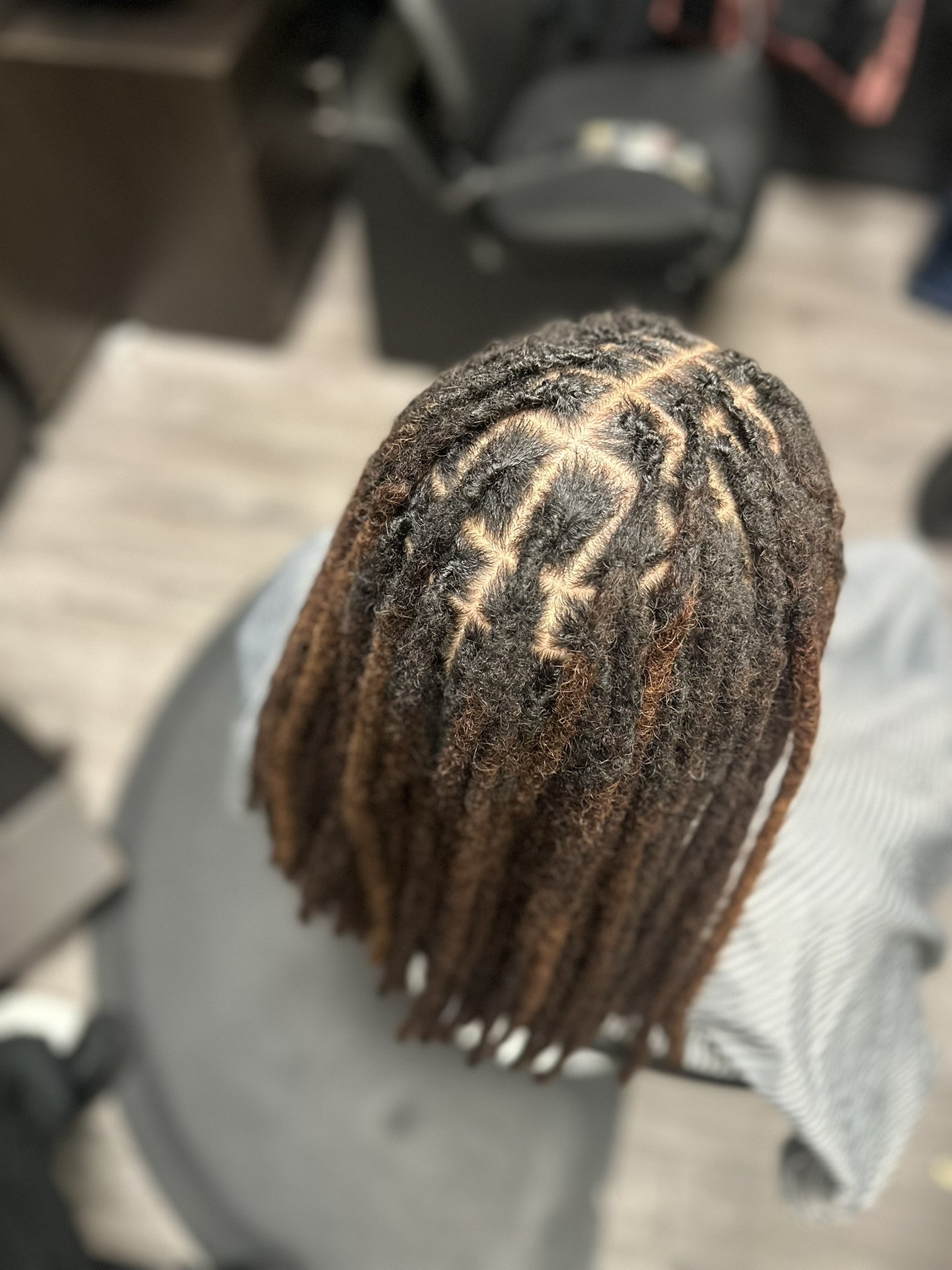 Top view of a person with blond, twisted locs hairstyle, sitting in a salon chair.