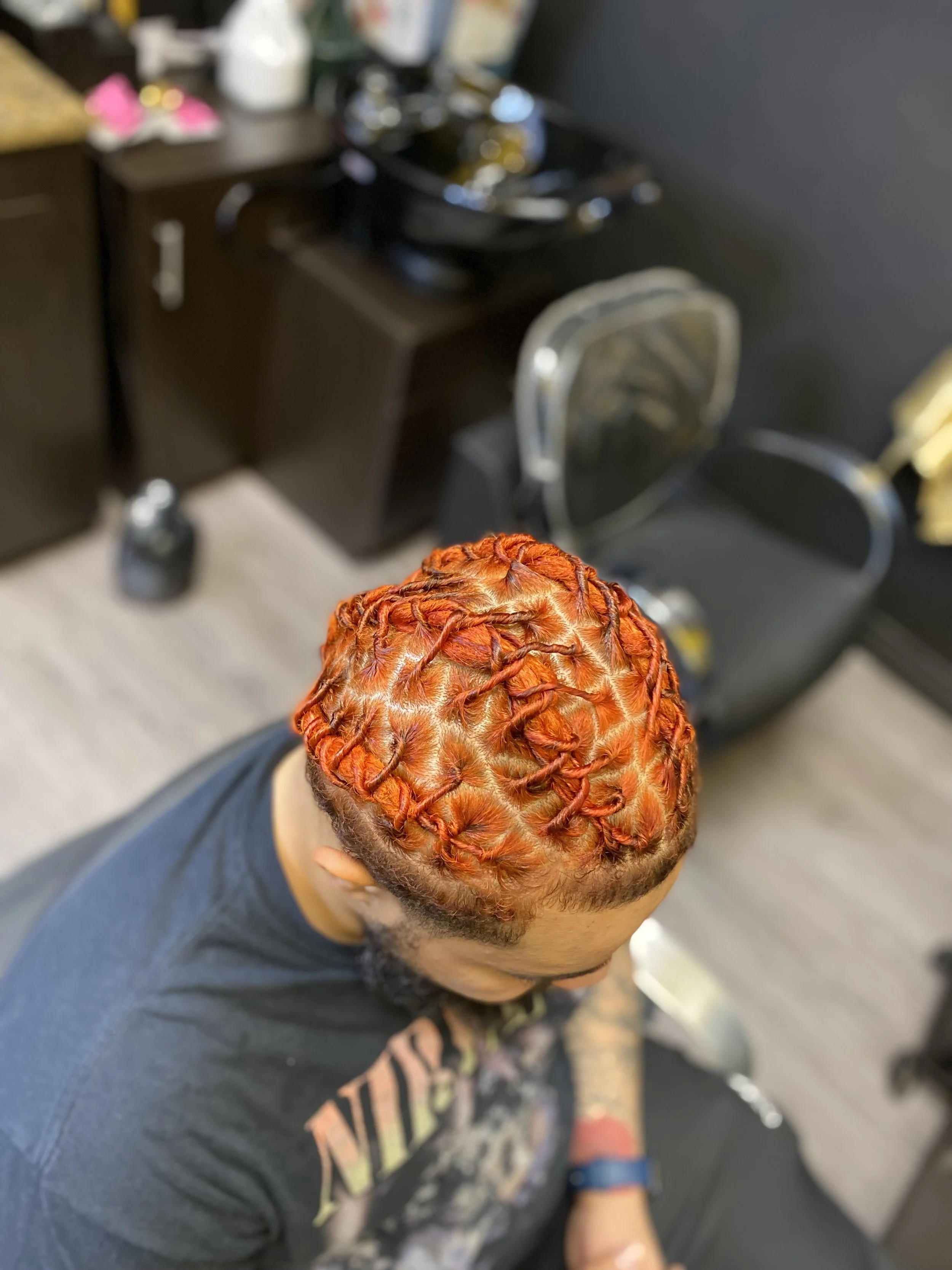 A person with short hair styled in bright orange and red knot twists, sitting in a salon chair.