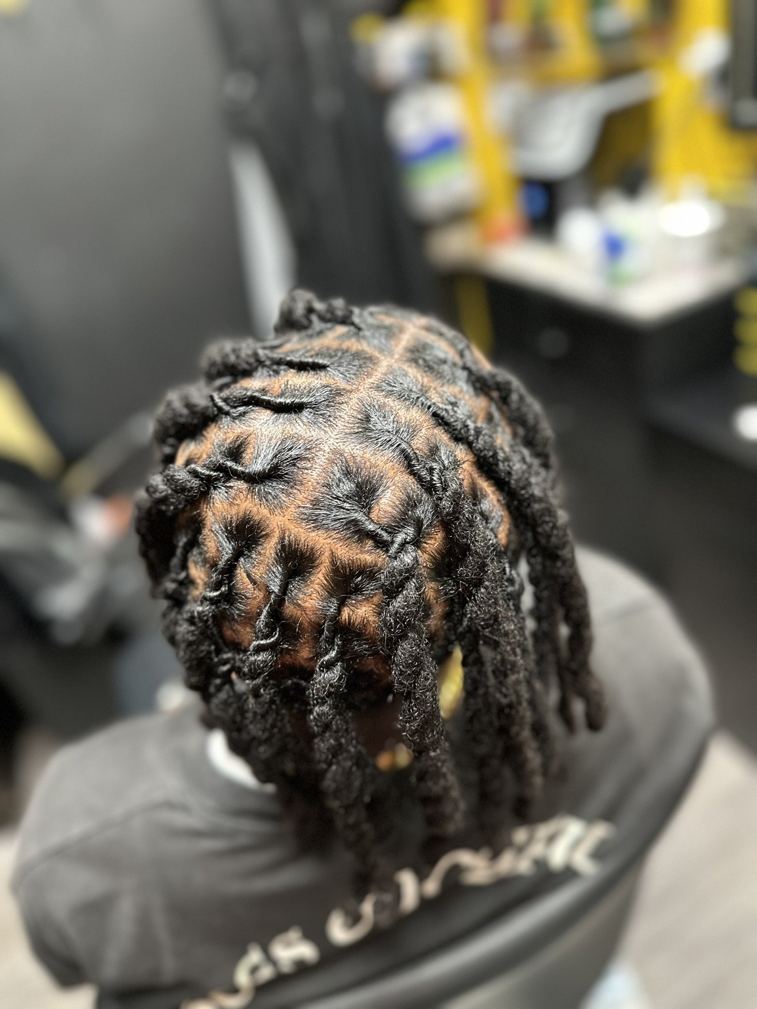 A person with styled dreadlocks sitting in a salon, with hair sections sectioned off for styling.