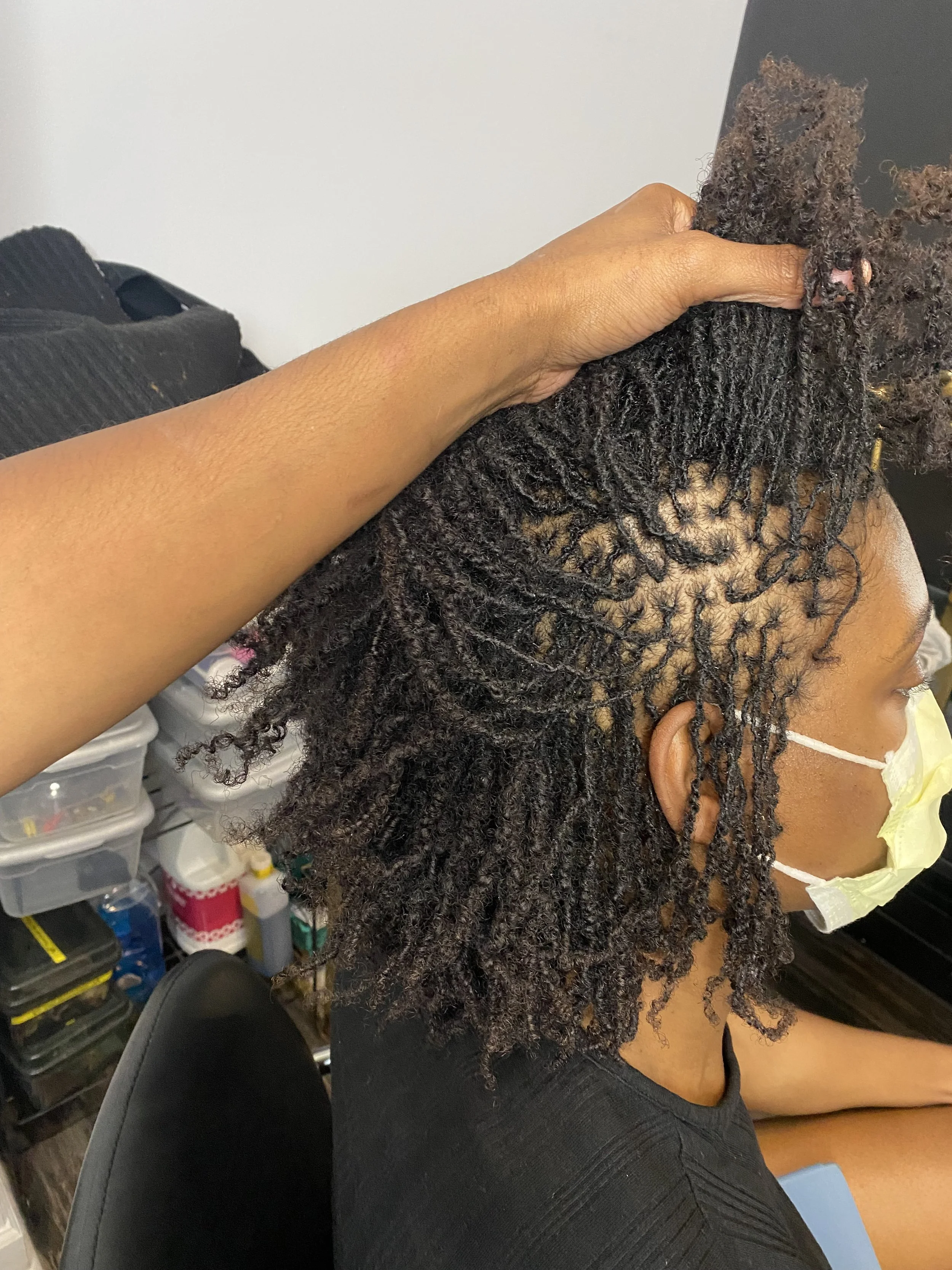 Person with curly, twisted hair getting a professional hairstyle with a hand holding their hair upwards.