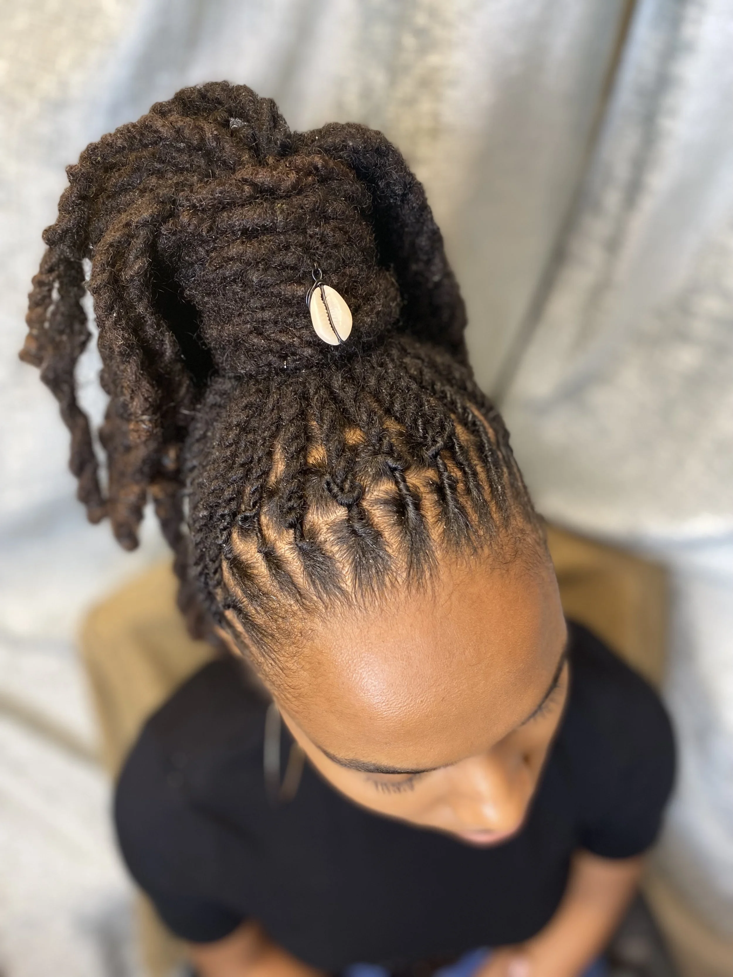 A woman with neatly styled dreadlocks tied up in a high bun decorated with a shell hair accessory.