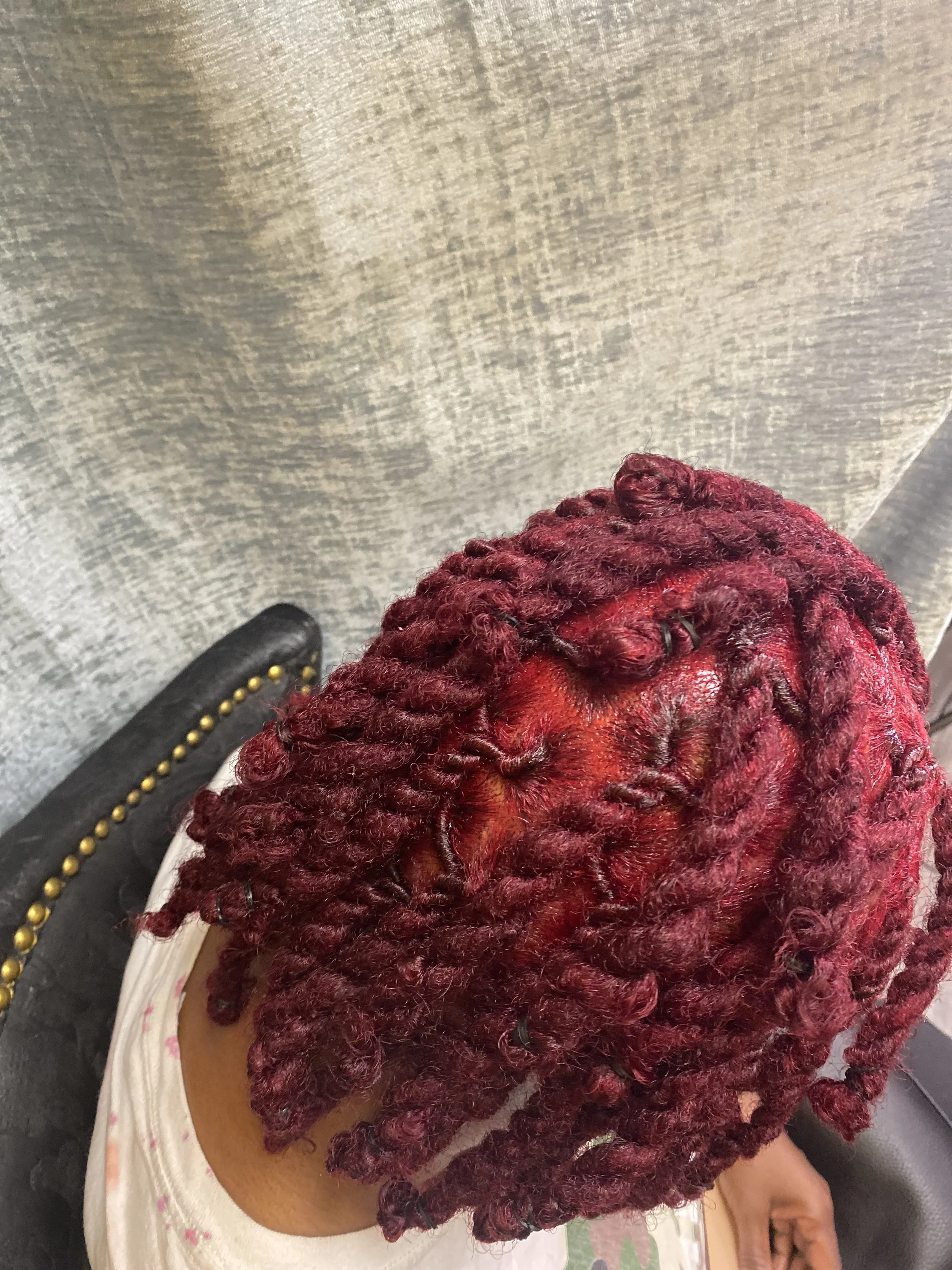 Top view of a person's head with freshly styled red hair in tight twists, sitting in a salon chair.