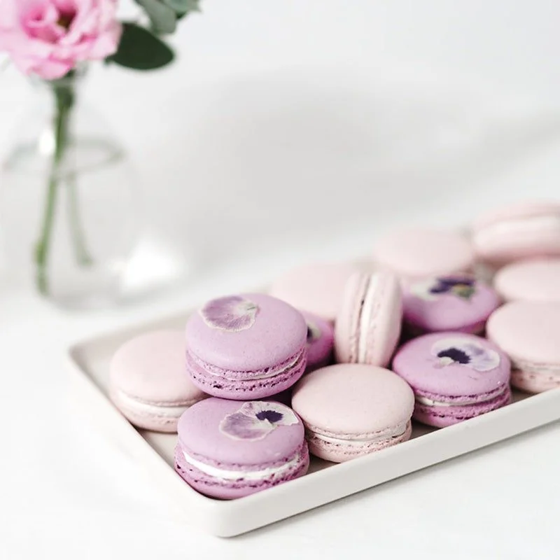 Koristeltuja vaaleanpunaisia ja valkoisia macaroneja tarjoiluastiassa