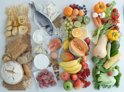 Assorted fresh fruits, vegetables, dairy products, grains, and fish arranged on a table.