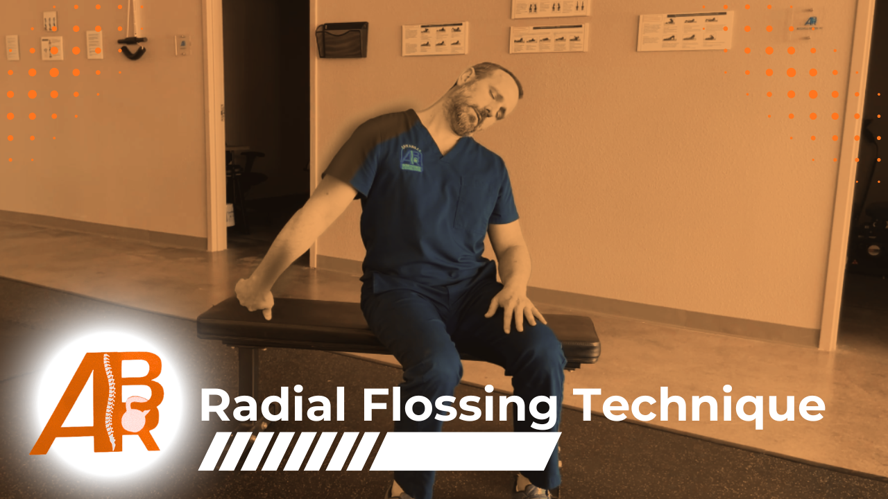A healthcare professional sitting on a black treatment table, demonstrating a radial flossing technique with his hand while in a medical office or therapy room.