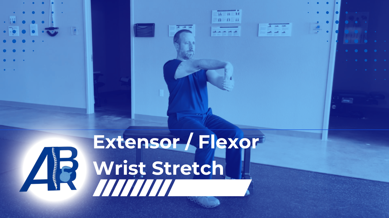 Man performing wrist stretch exercise while sitting on a bench in a therapy or training room, with exercise equipment and informational posters on the wall.