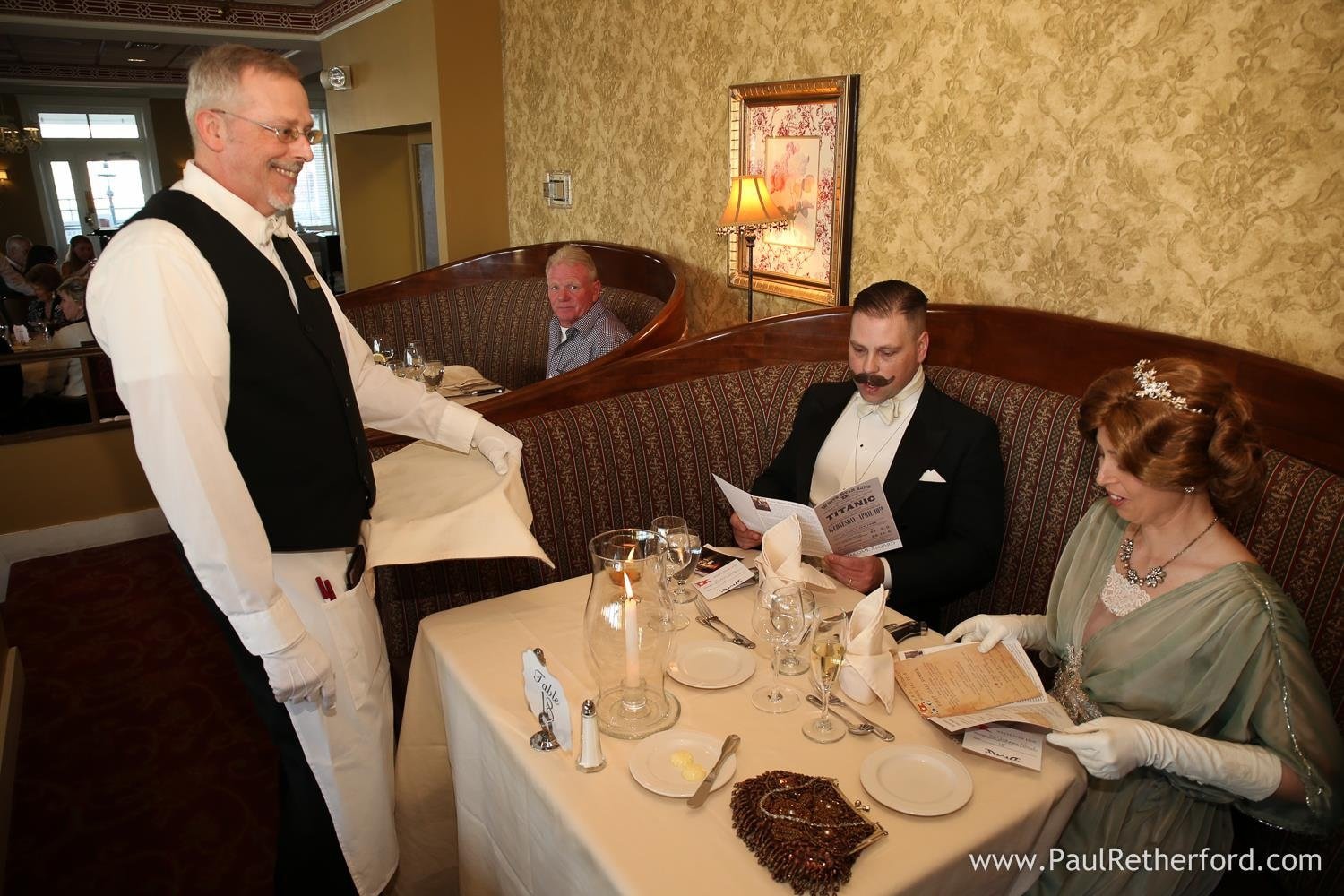 Man and woman in Edwardian attire being served by a waiter in a restaurant. Probably at Edwardian event.