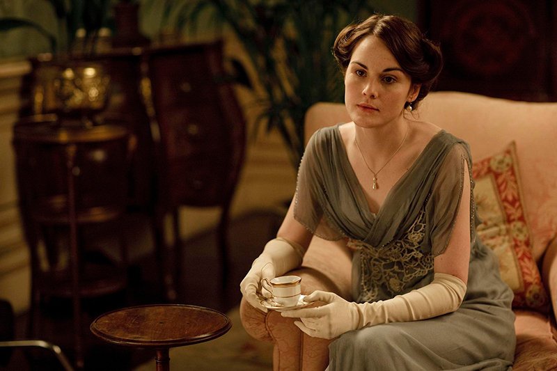 A picture form Downton Abbey film - Lady Mary in the green dress sitting on a sofa and thinking.