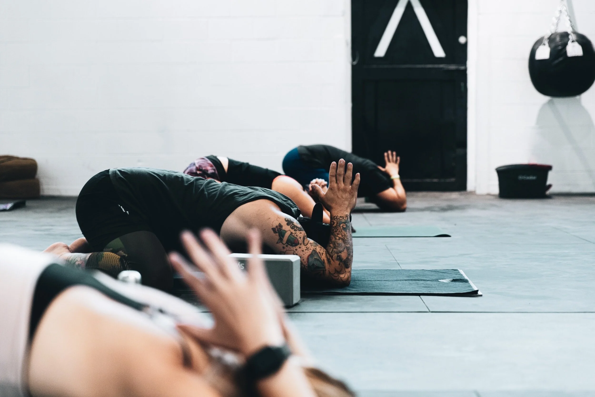 People doing yoga in a gym, performing a resting pose on mats.