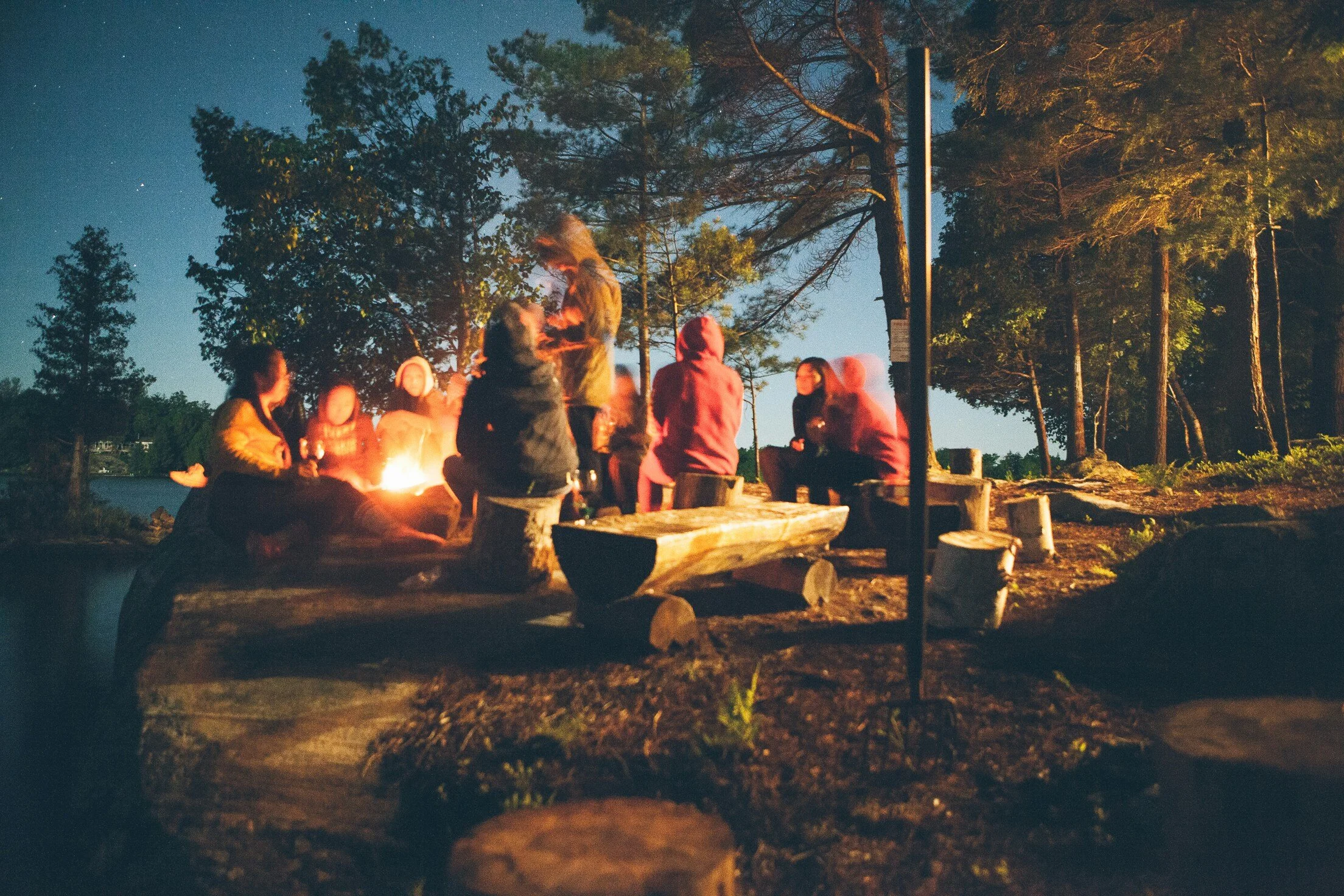 Group of people sitting around a campfire in a forest at night.